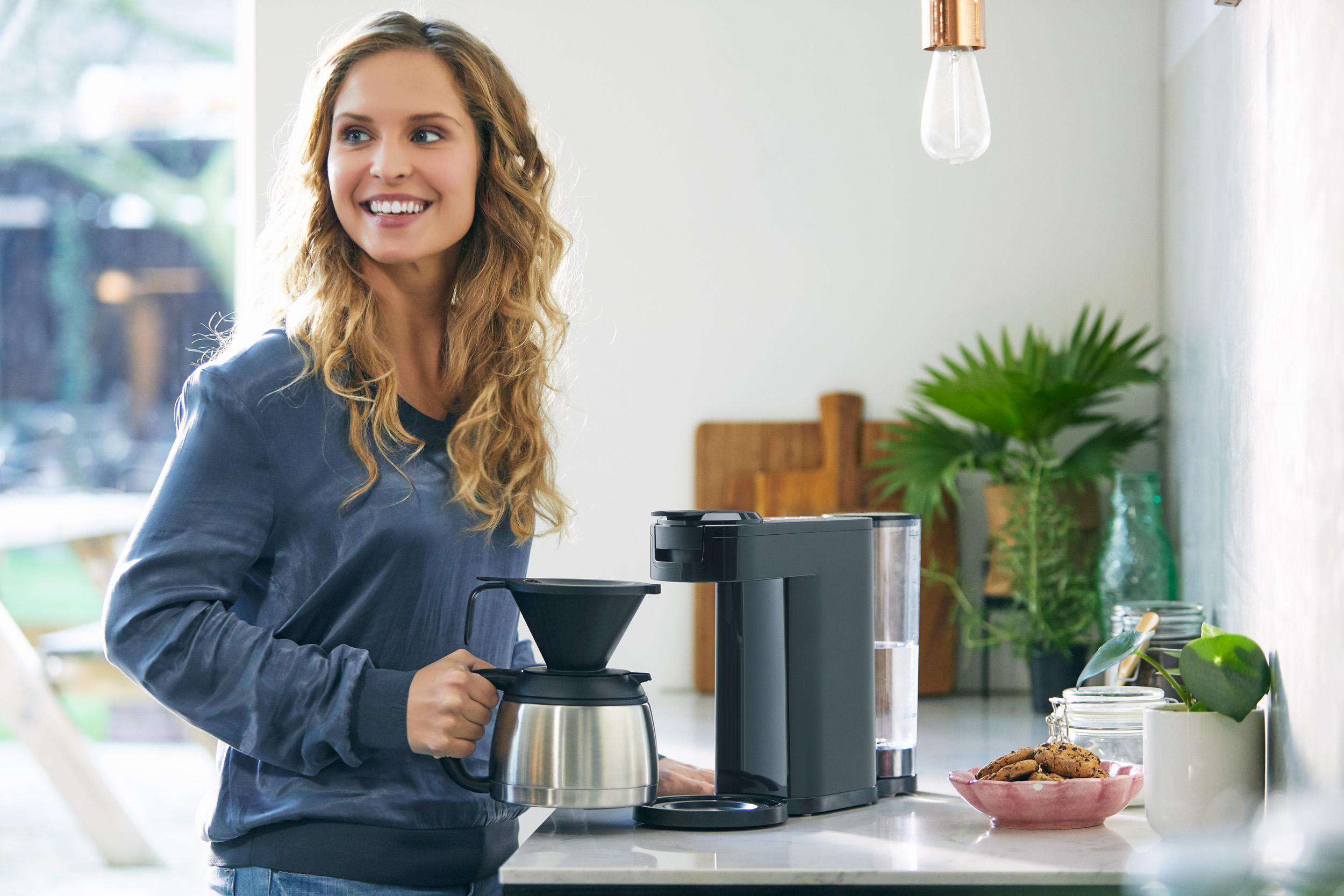 Frau in der Küche macht Kaffee, lächelt, mit Kaffeemaschine.