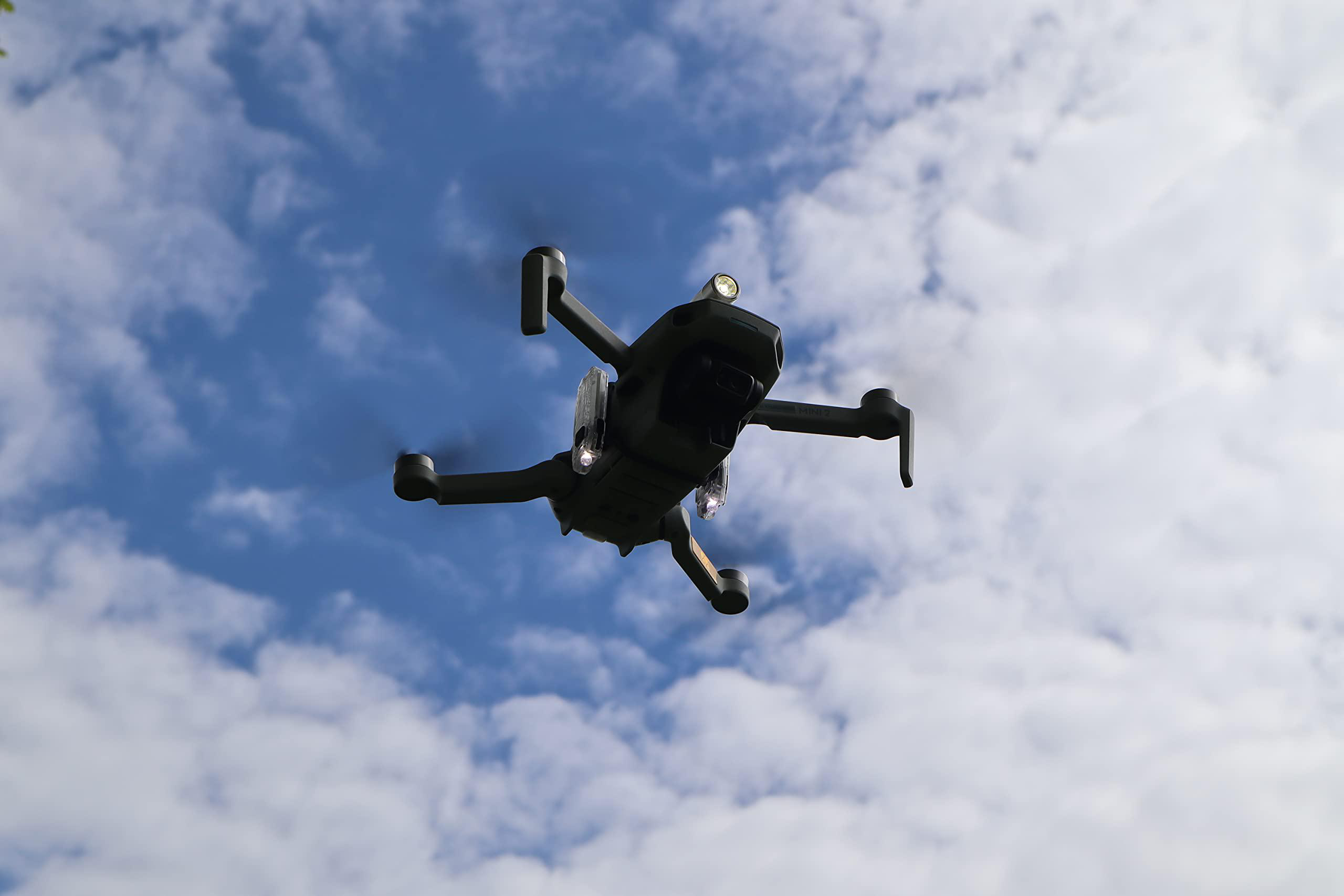 Eine schwarze Drohne fliegt in einem blauen Himmel mit weißen Wolken, nach oben geneigt.