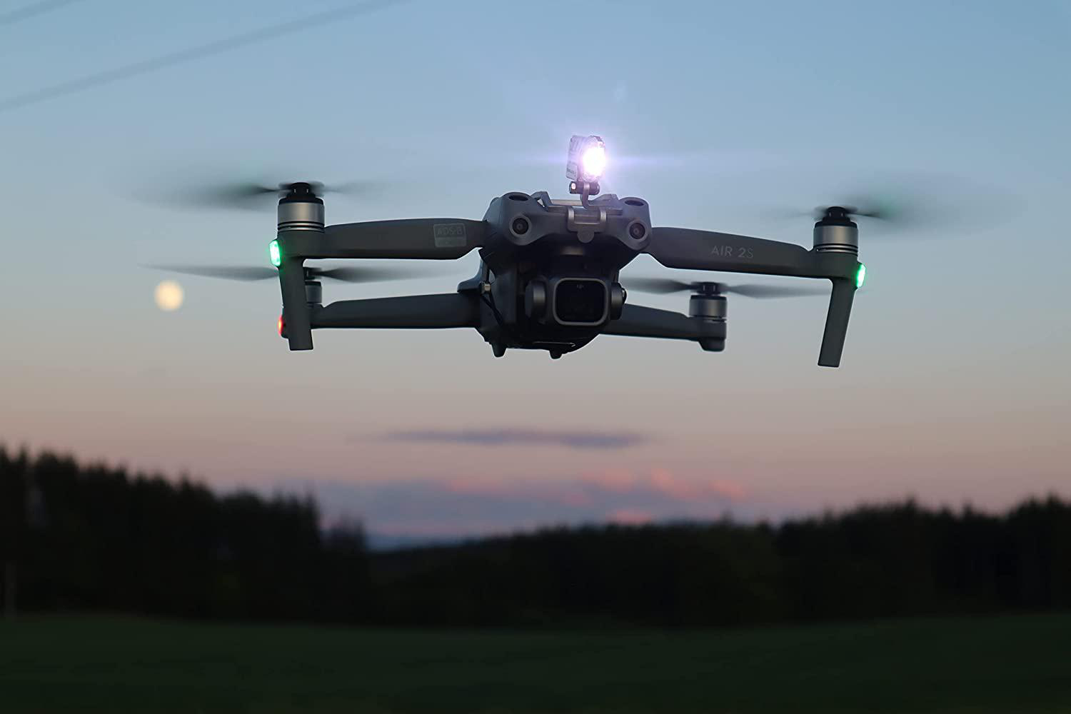 Drohne im Flug in der Abenddämmerung, mit Lichtern. Im Hintergrund der Sonnenuntergang.