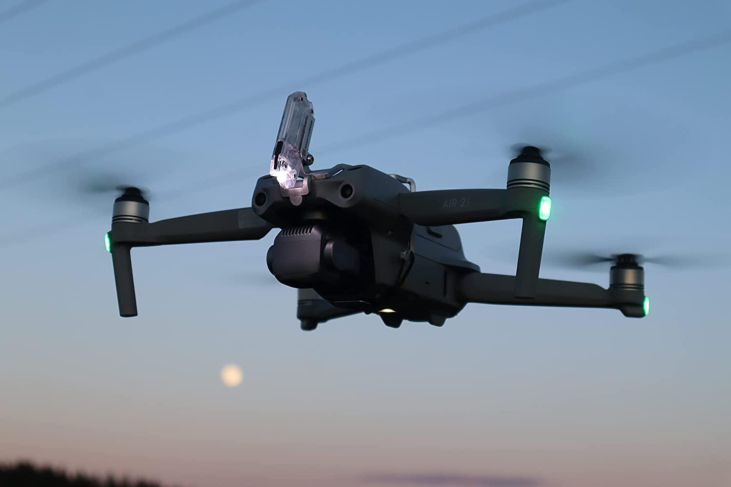 Eine Drohne fliegt nachts mit eingeschaltetem Licht. Der Himmel ist dunkelblau.