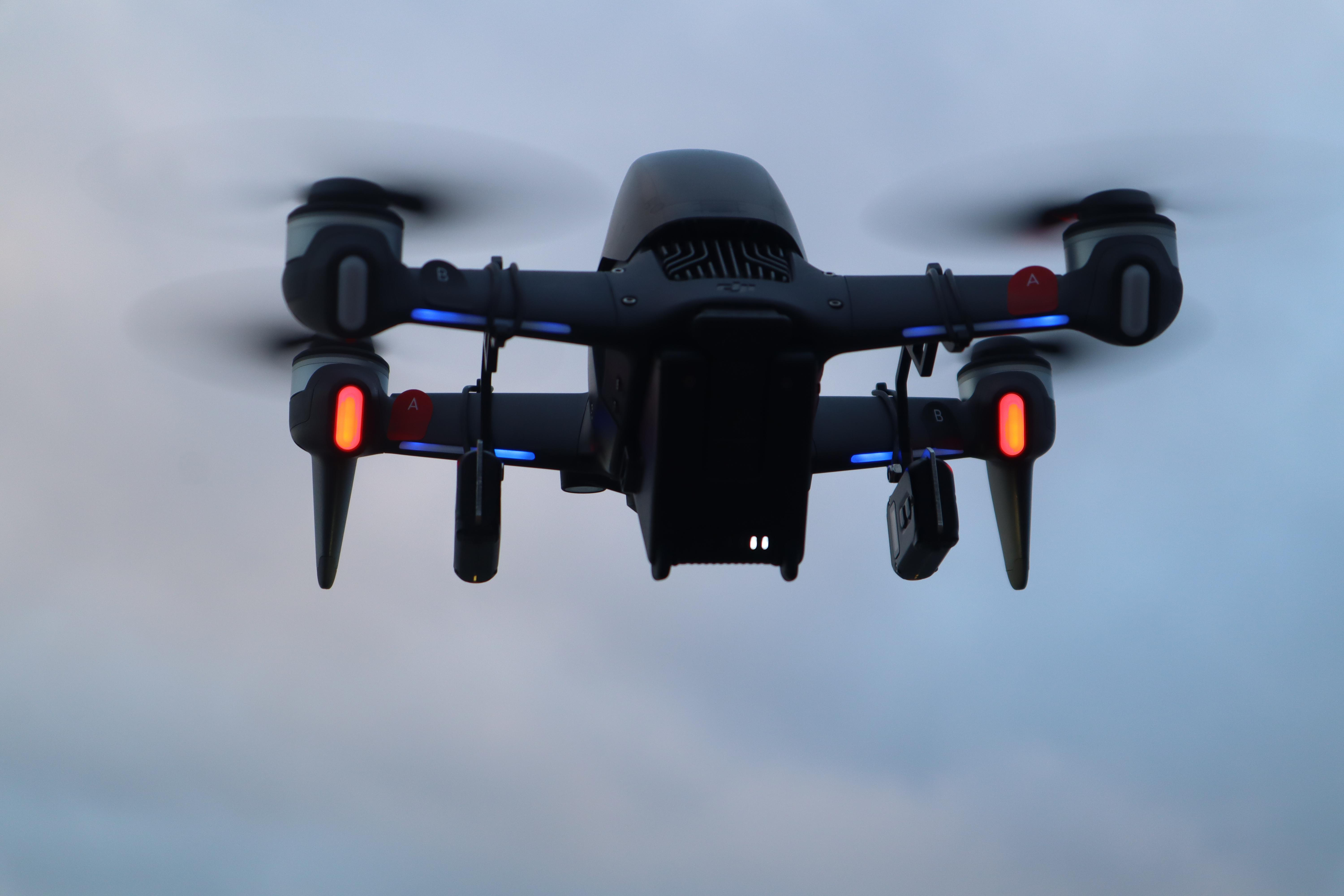 Eine schwarze Drohne, die mit beleuchteten Lichtern am Himmel fliegt.