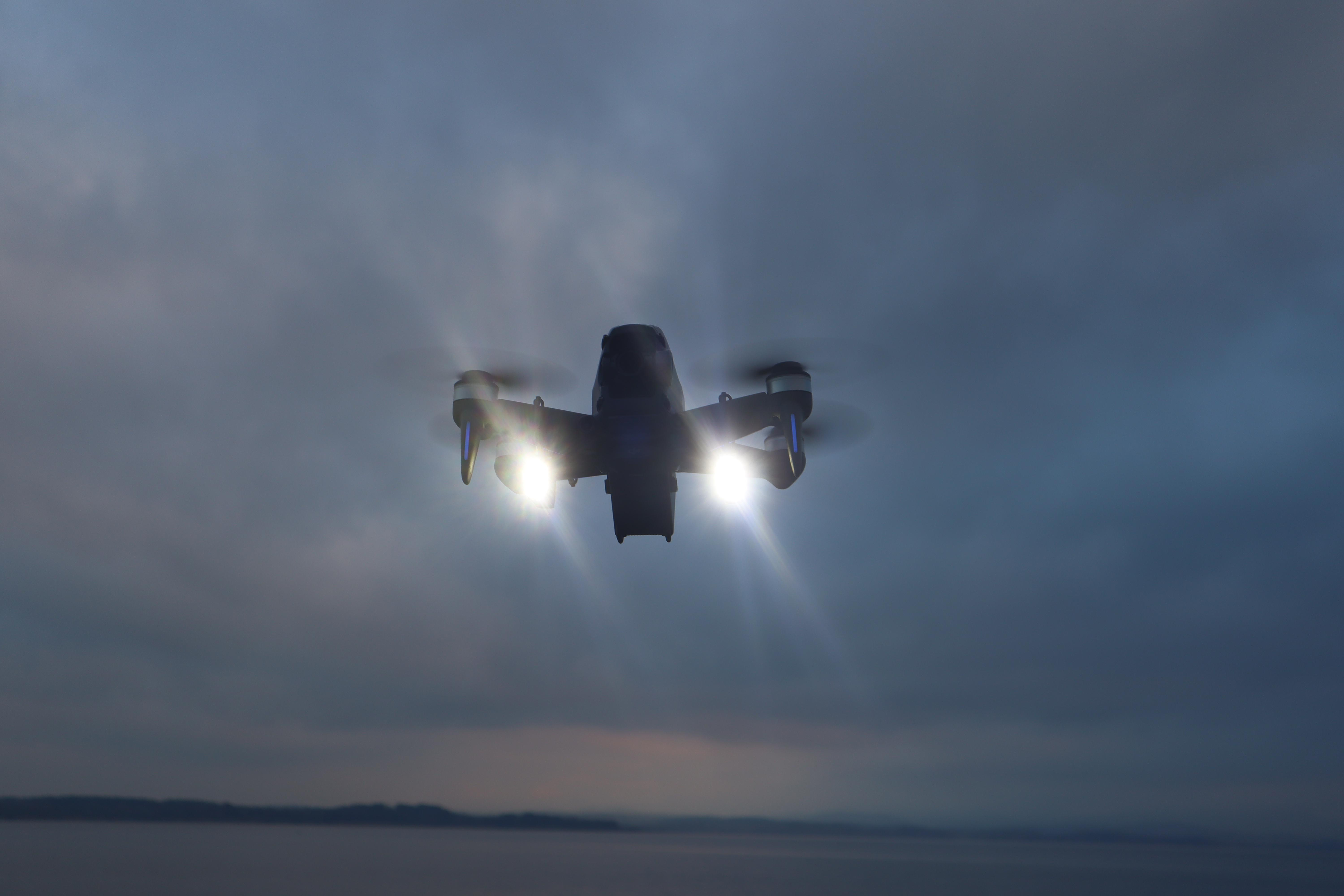 Drohne fliegt in einem bewölkten Himmel. Lichter an der Front sind beleuchtet.