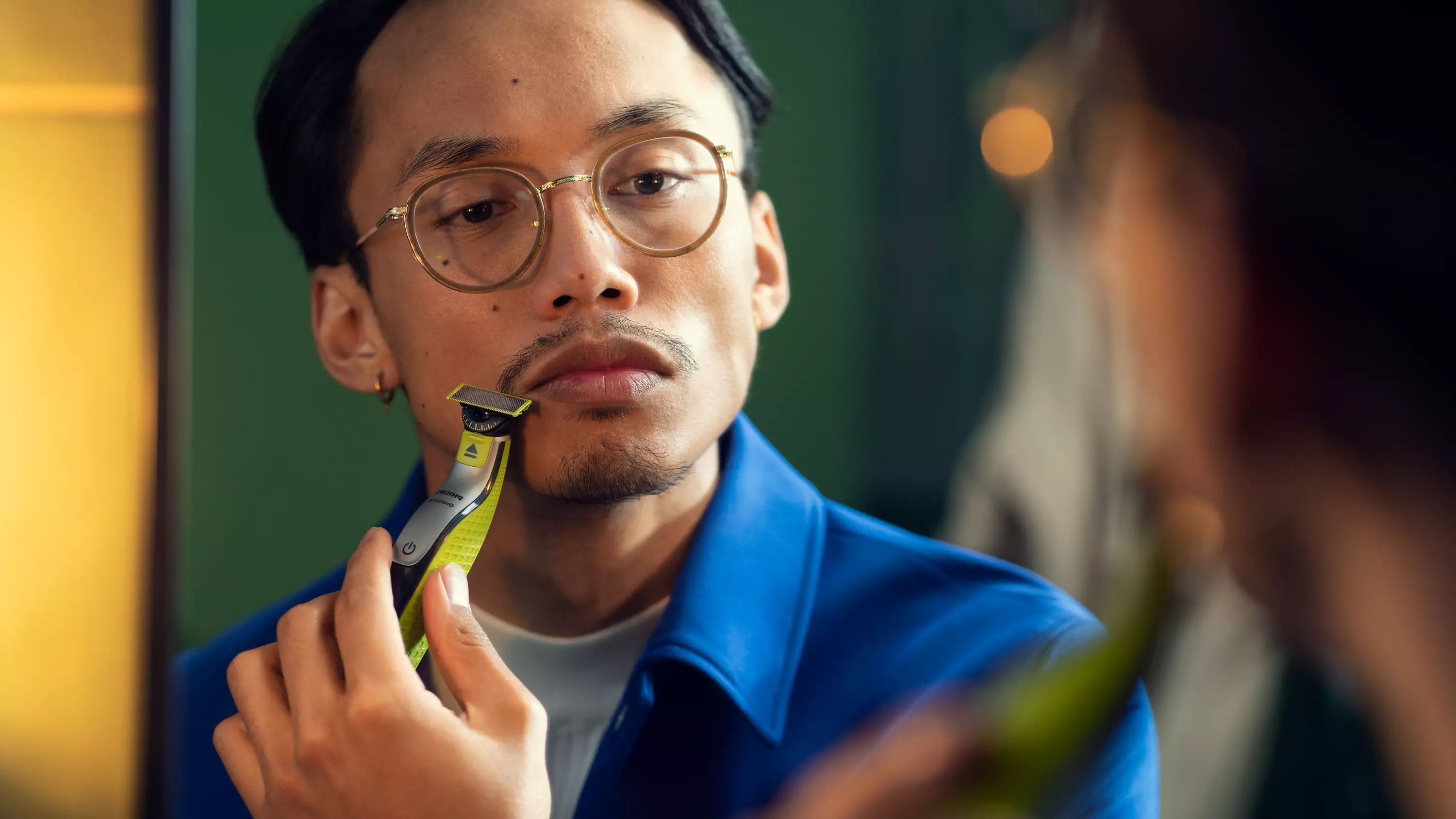 Homme se rasant la moustache avec un rasoir électrique dans un miroir.