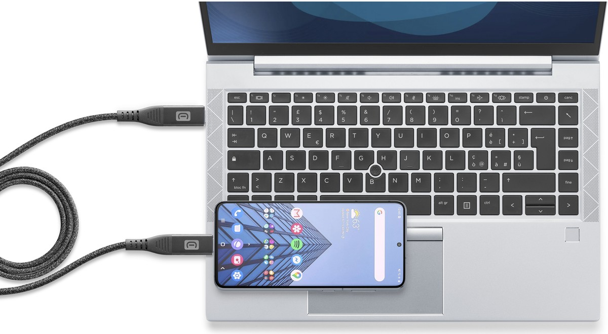 Laptop mit Smartphone, das über ein Kabel verbunden ist. Beide liegen auf einer weißen Oberfläche.