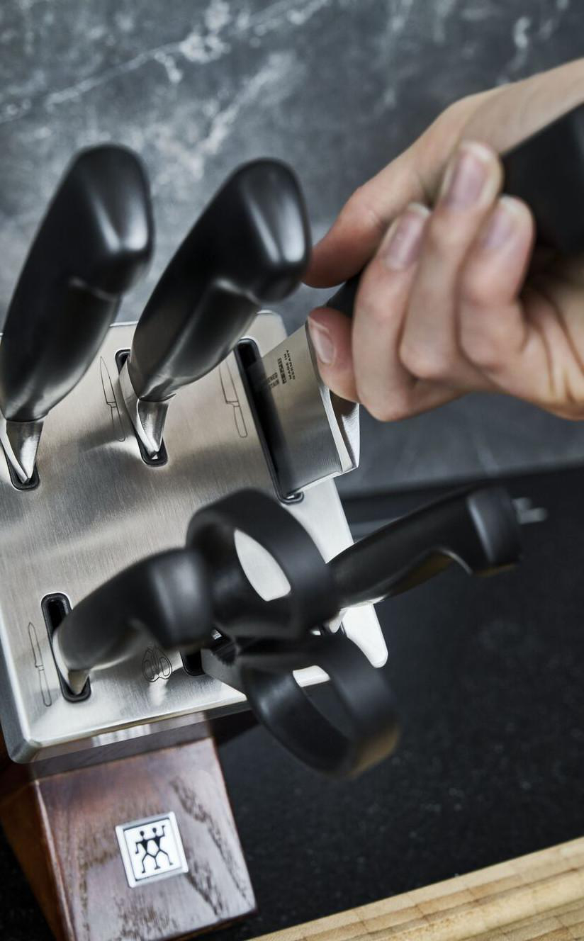 Eine Hand steckt ein Messer in einen Block mit anderen Messern. Edelstahl.