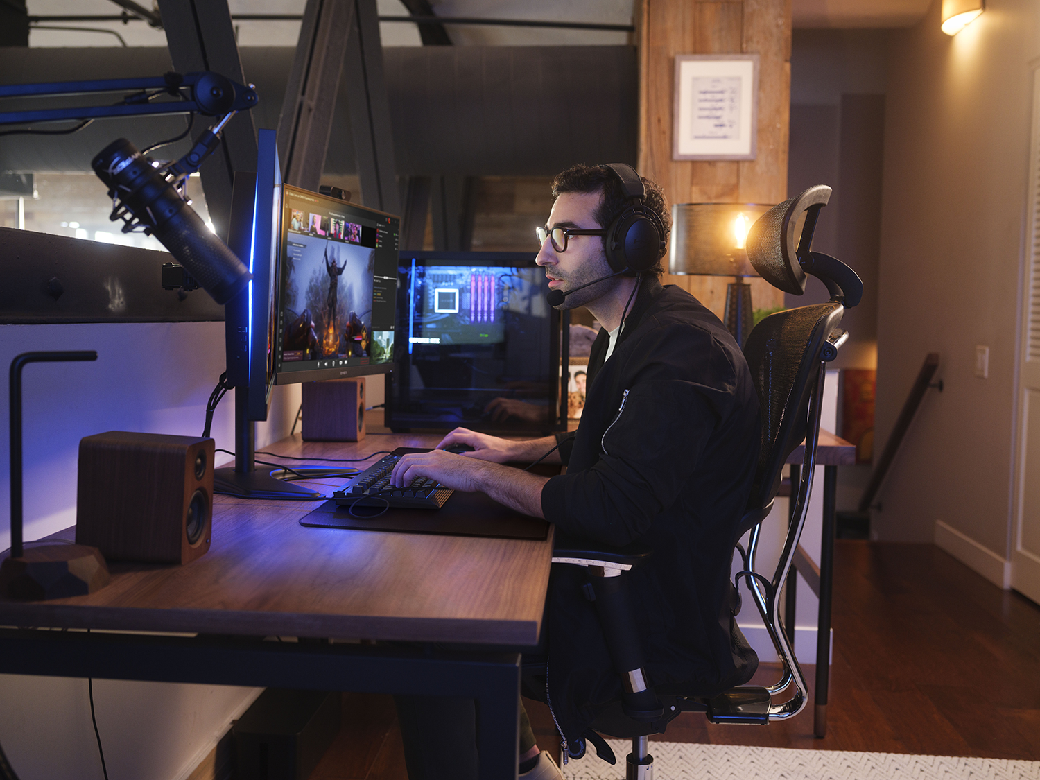 Een man met een bril en een headset zit aan een bureau met een computer.