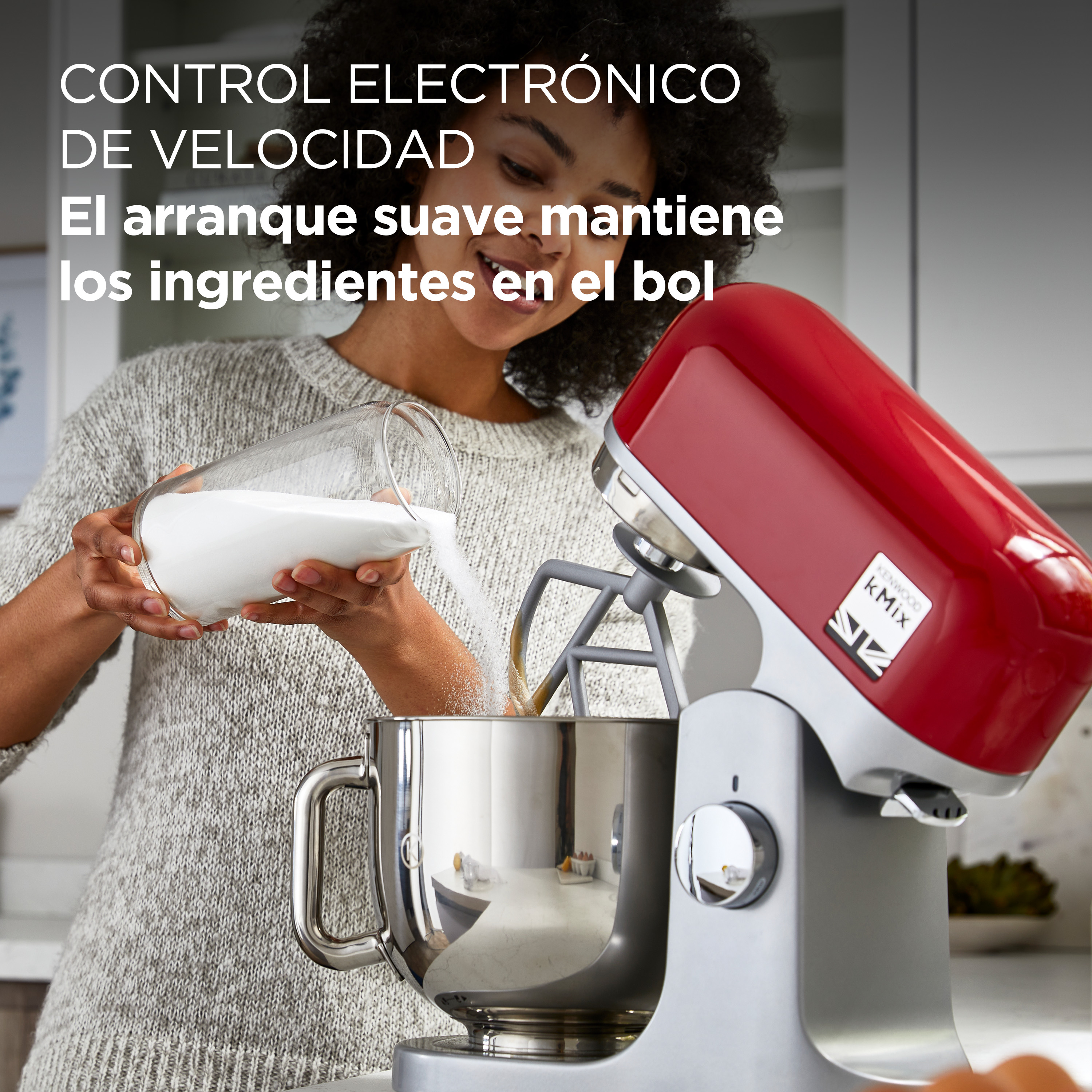 Mujer añadiendo azúcar a un bol con una batidora KitchenAid roja, fondo blanco.