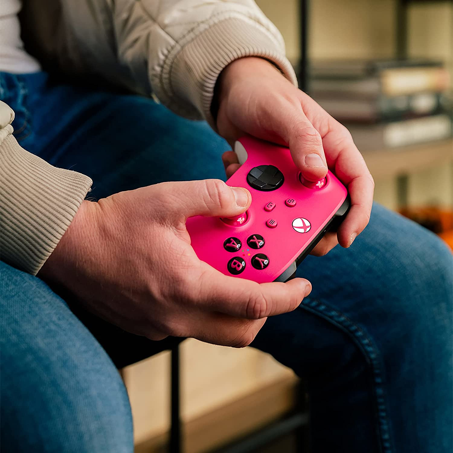 Mains tenant une manette de jeu vidéo rose avec des boutons. Un jean bleu est visible.