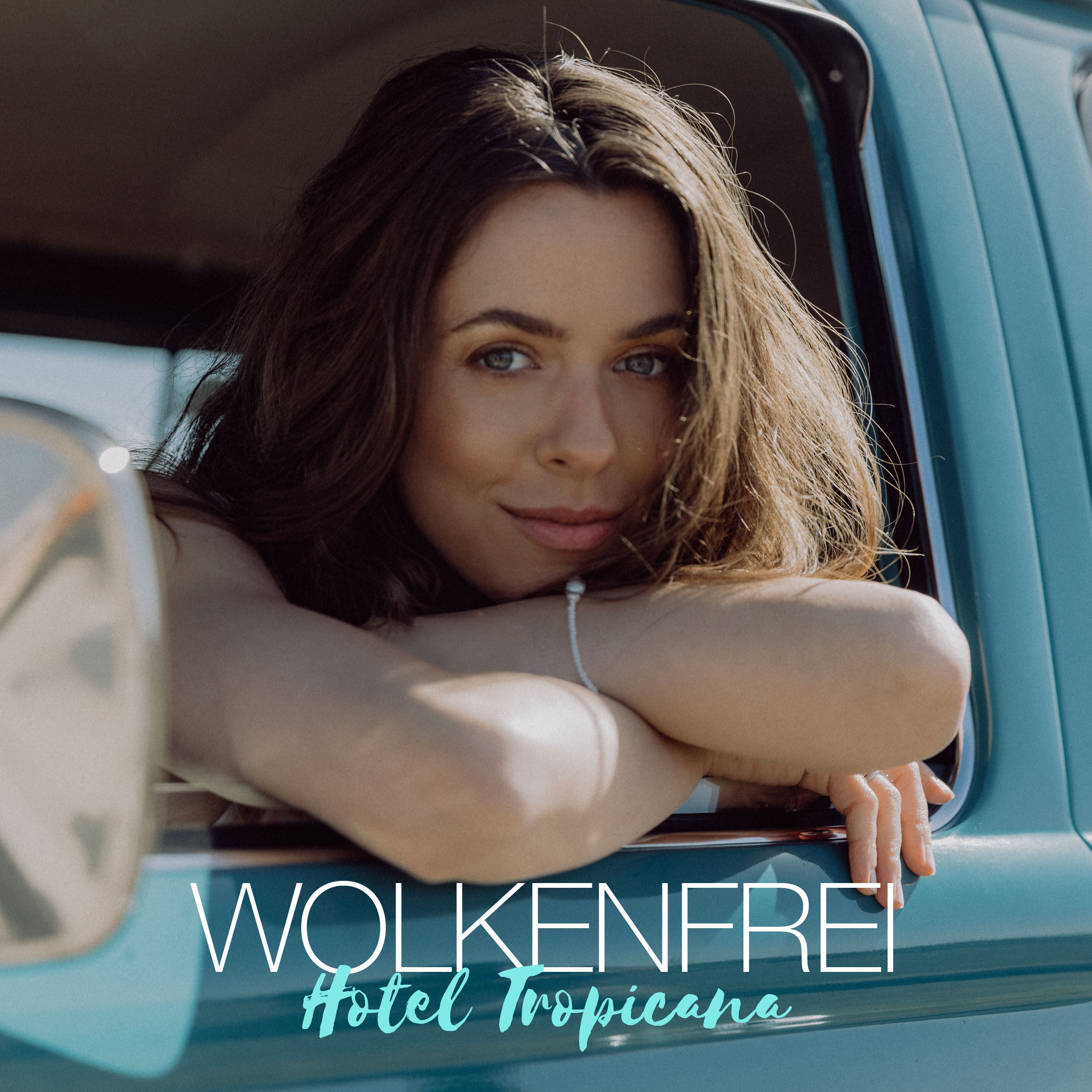 Eine Frau in einem Auto, die mit einem Lächeln in die Kamera schaut. Text: WOLKENFREI Hotel Tropicana.