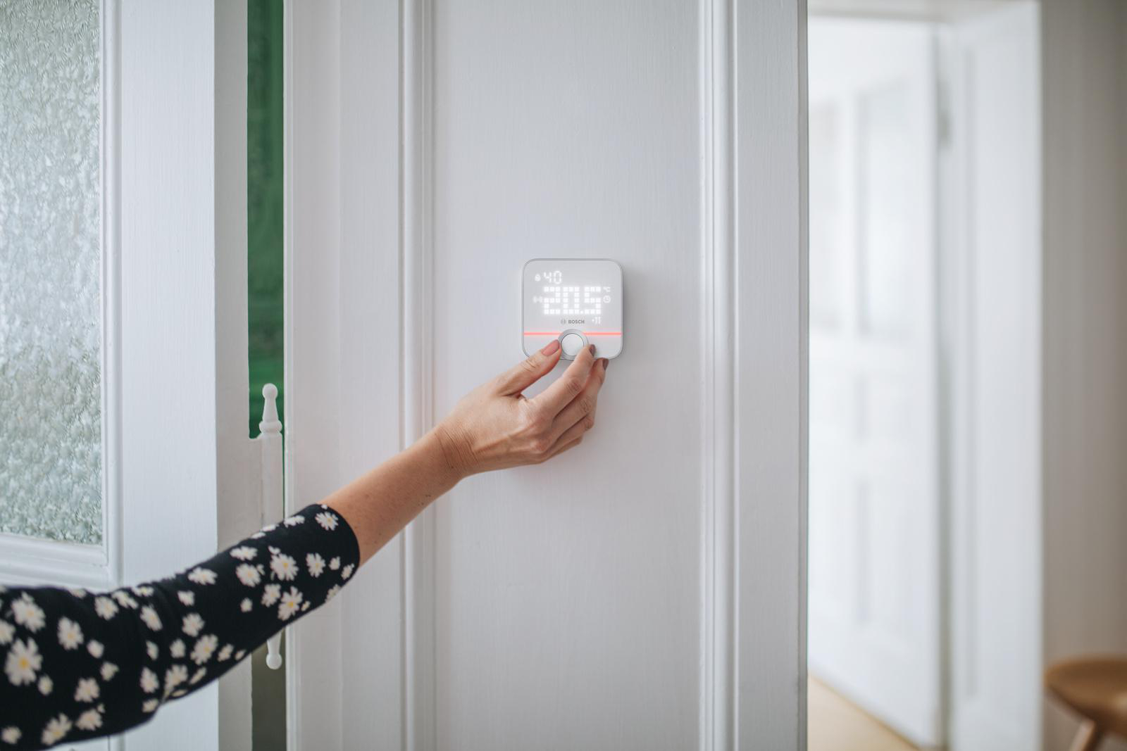 Hand einer Frau, die ein Smart-Home-Gerät an einer weißen Wand in der Nähe einer Tür einstellt.