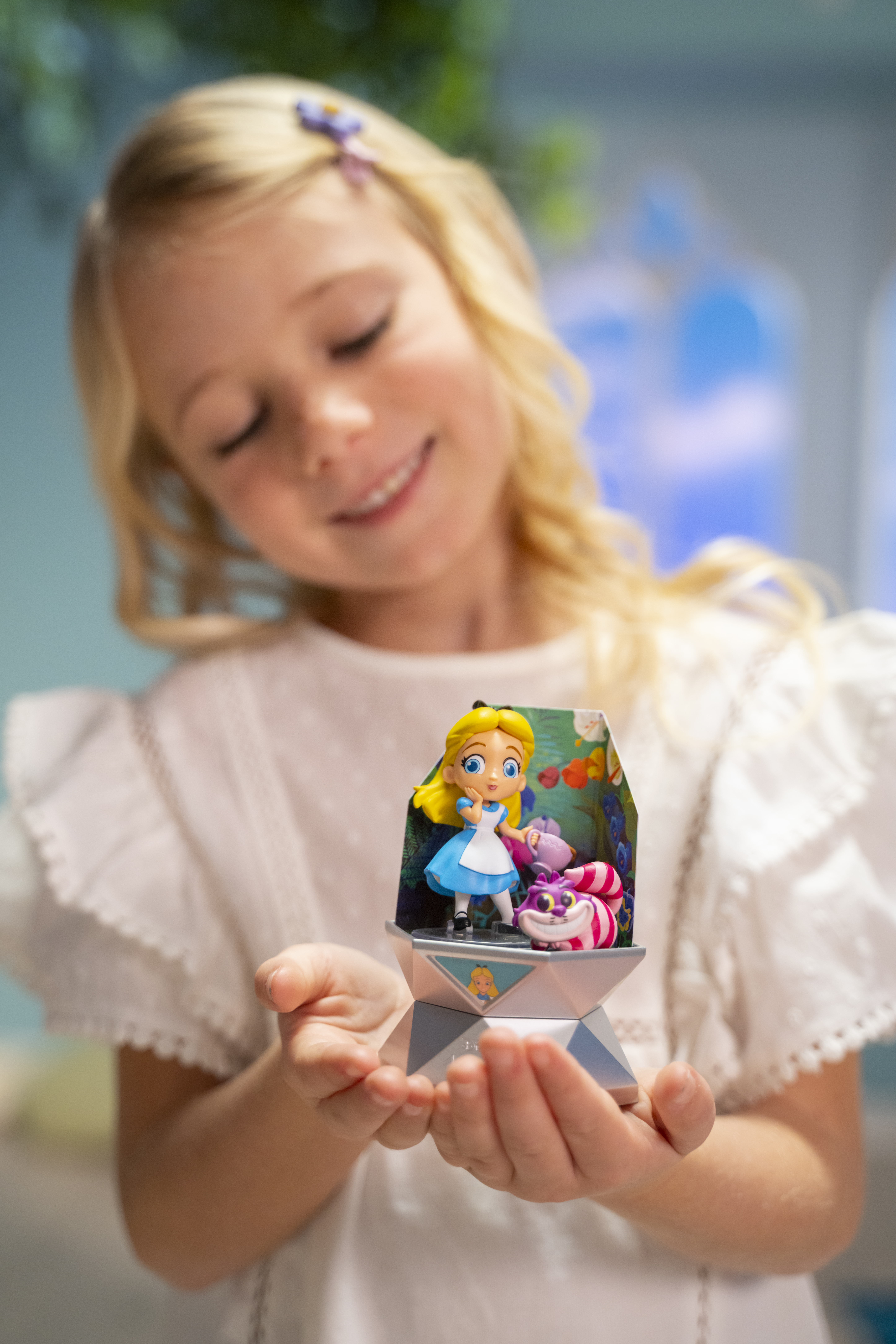 Blondes Mädchen hält Alice im Wunderland-Figur. Hintergrund enthält eine blaue Szene.