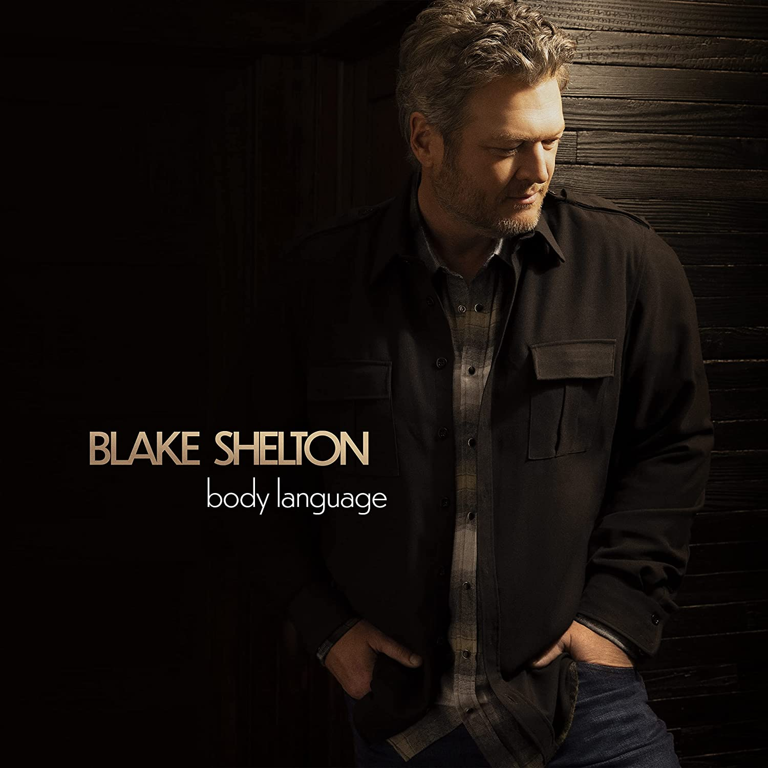 Blake Shelton album borító. Blake Shelton fekete dzsekiben, sötét falnak dőlve. 'Body Language'.