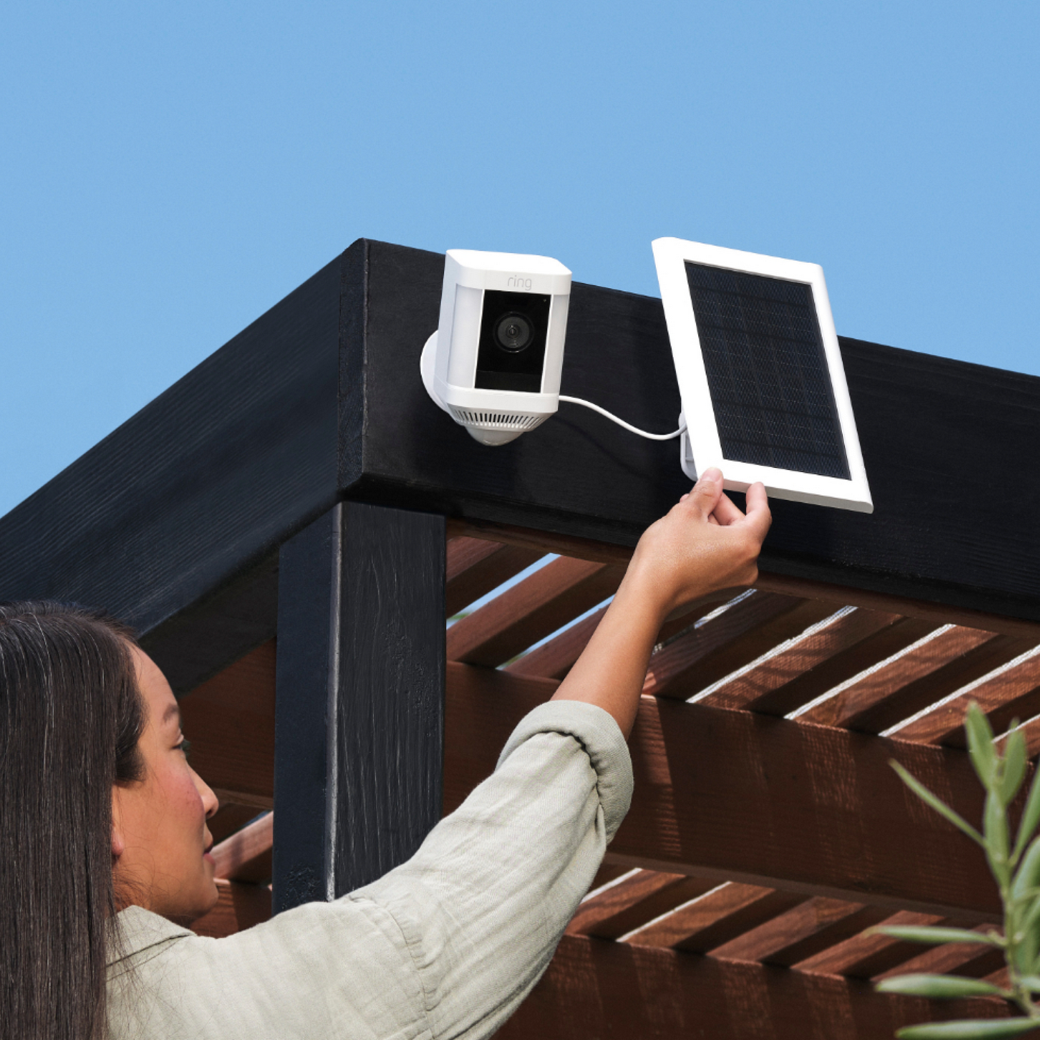 Woman installing a security camera on a pergola. The camera is white and solar panel too.