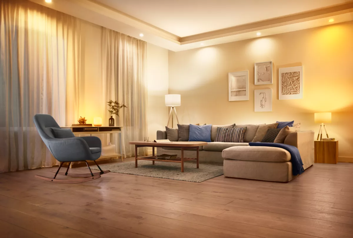 Salón con iluminación cálida, sofá, sillón, mesa de centro, cuadros en la pared y suelo de madera.