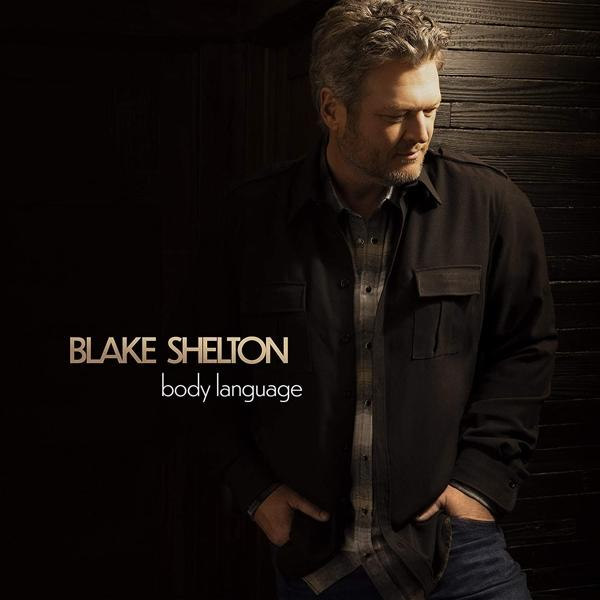 Blake Shelton kockás inget és dzsekit visel, egy sötét fa falnak dől. A szöveg: body language.