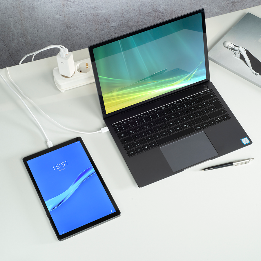 Tablet and laptop on white desk. Tablet shows time 15:57. Charger and power strip in the background.
