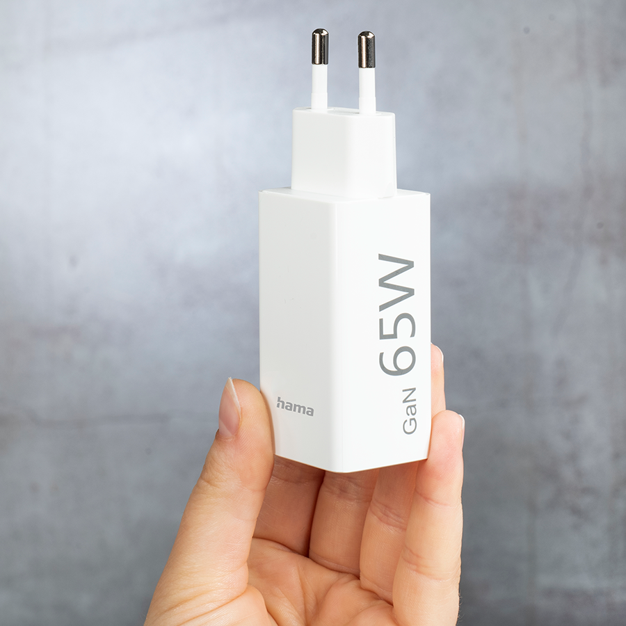 White 65W GaN charger with two prongs, held by a hand.