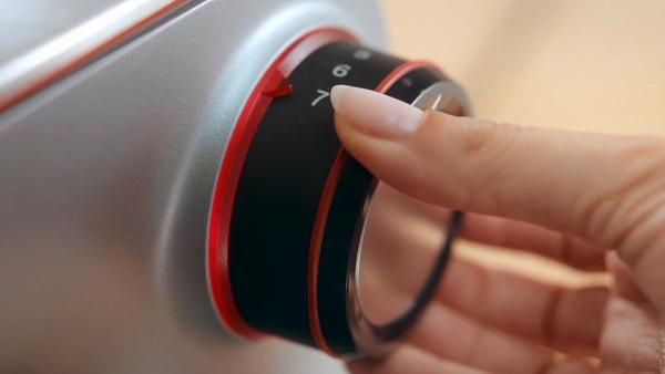 Nahaufnahme einer Hand, die einen Drehregler an einer silbernen Maschine dreht, mit roten Akzenten und der Zahl 7 im Fokus.