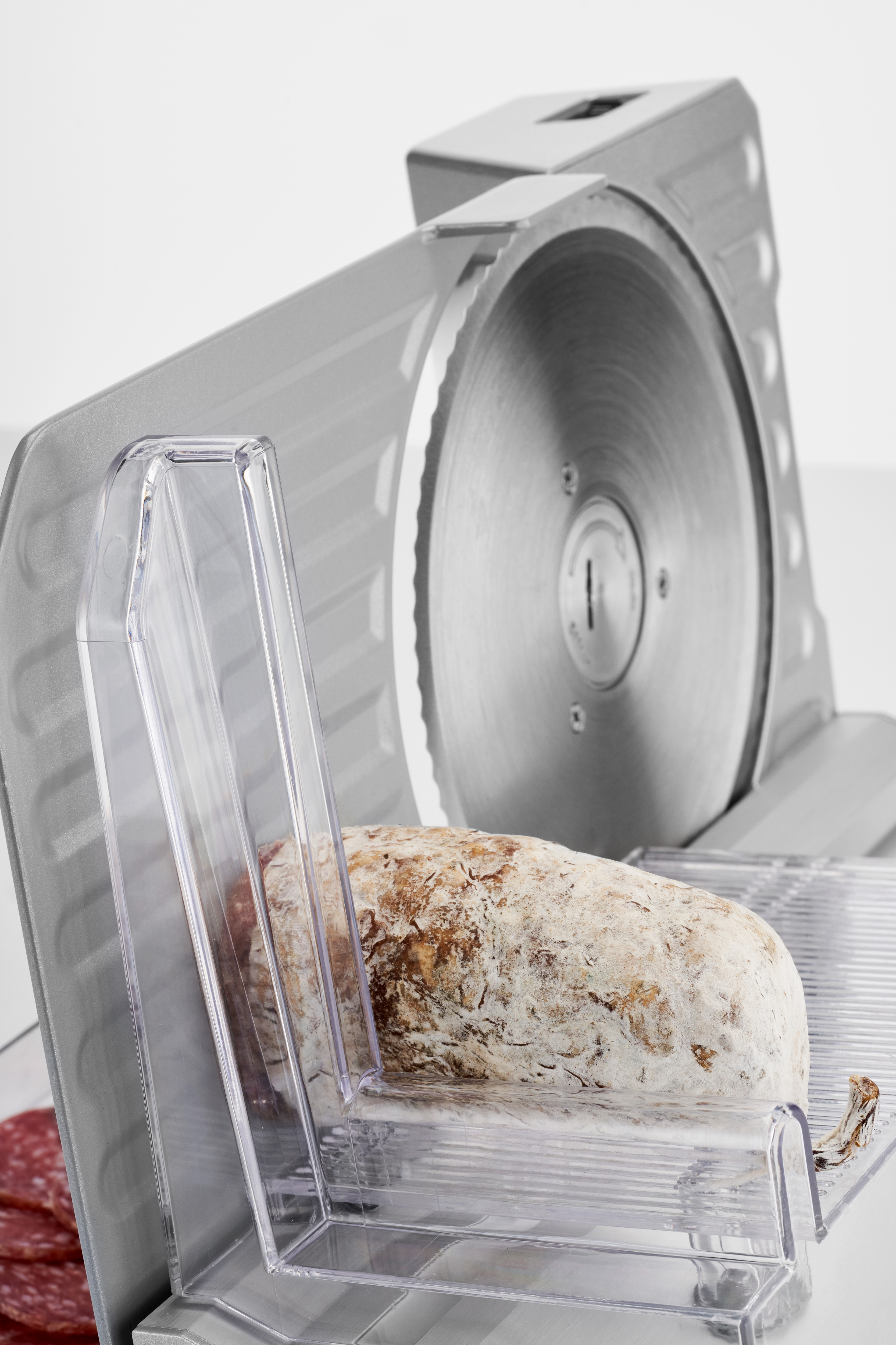 Une trancheuse à viande avec une grande lame circulaire et un morceau de salami.