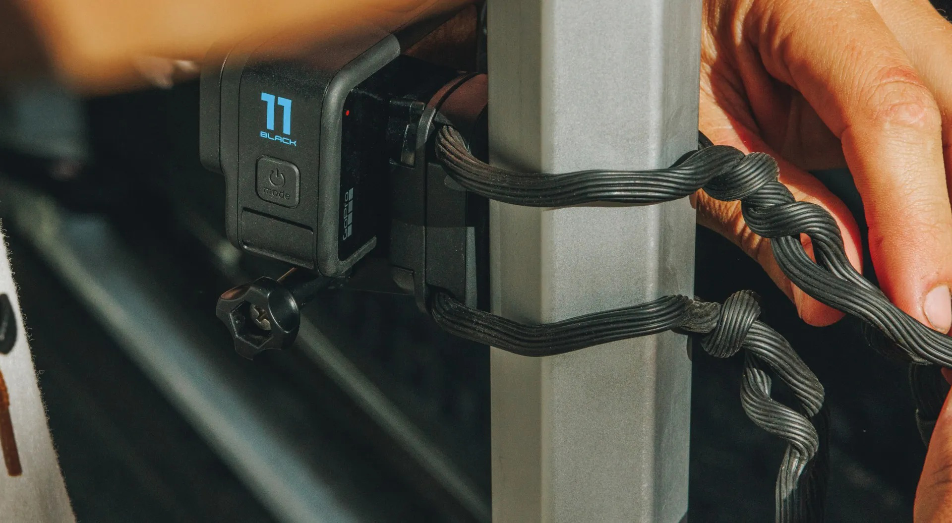 Hände, die eine schwarze GoPro-Kamera an einem Metallpfosten befestigen. Die Kamera zeigt 11 BLACK.