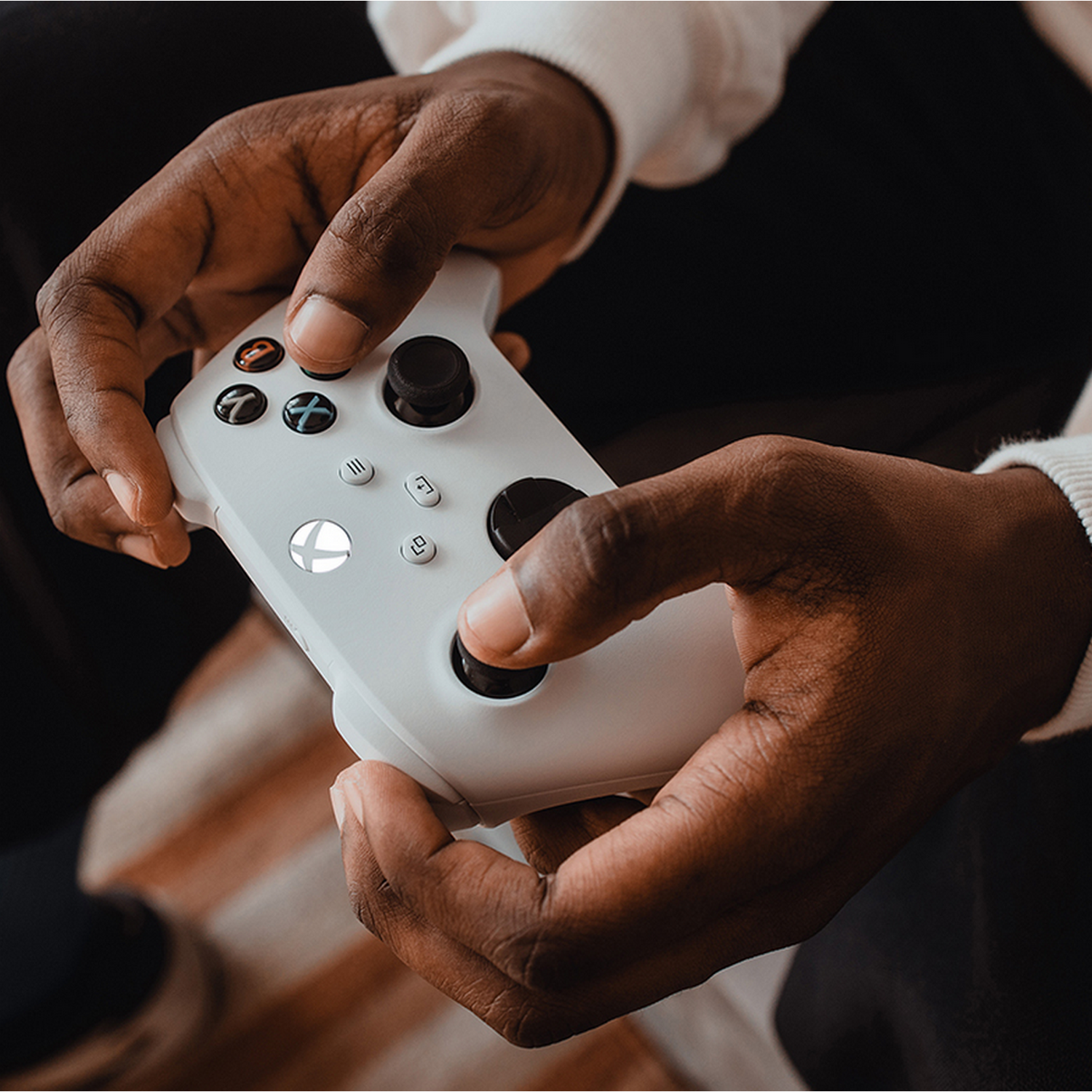 Handen die een witte Xbox-controller vasthouden. De controller heeft knoppen en joysticks.