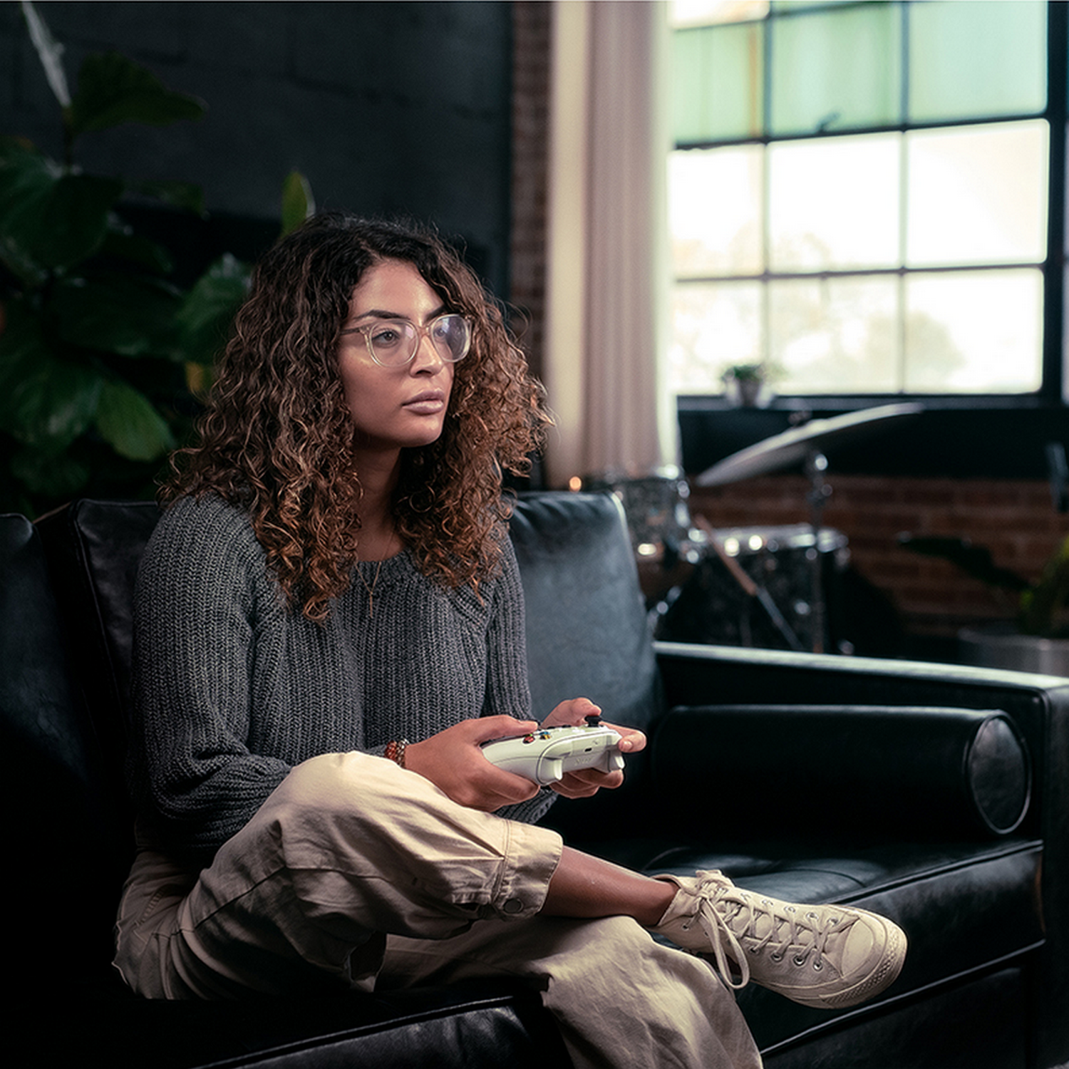 Een vrouw met een bril zit en speelt een videogame met een controller.