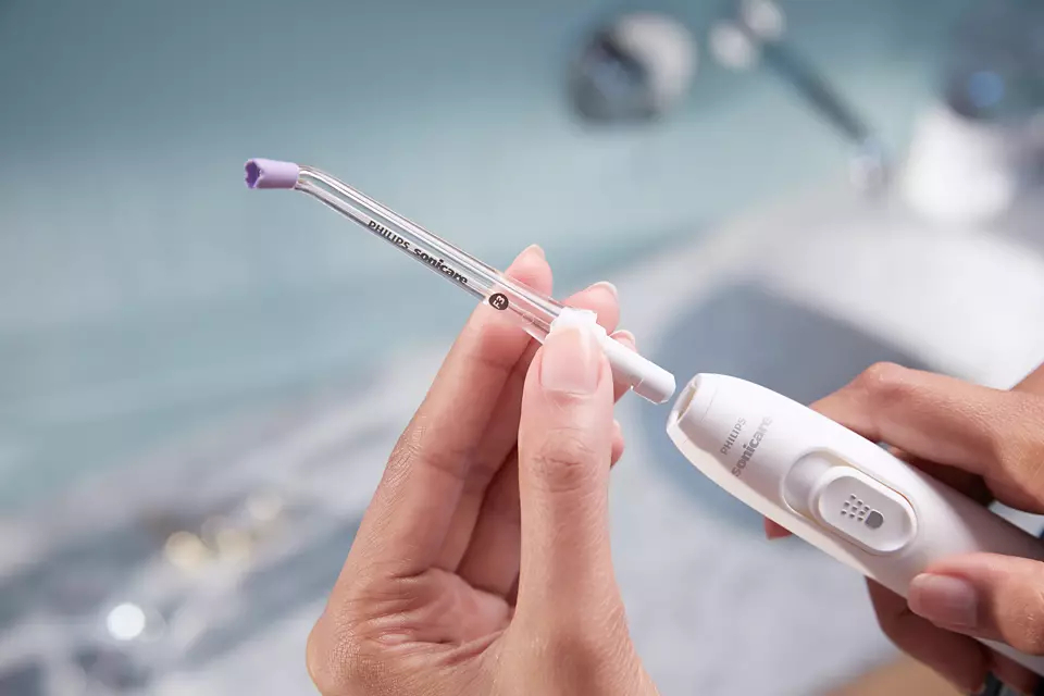 Eine Person hält einen Philips Sonicare Wasserflosser. Die Spitze wird an das Gerät angebracht.