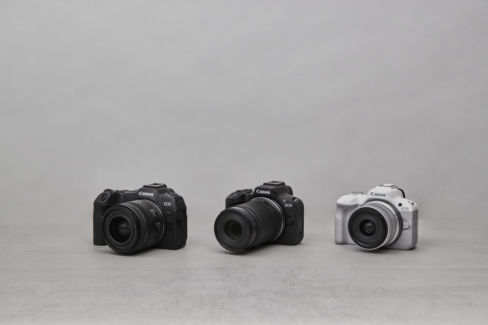 Drei Canon EOS Kameras auf grauer Oberfläche, jede mit Objektiv, die weiße rechts.