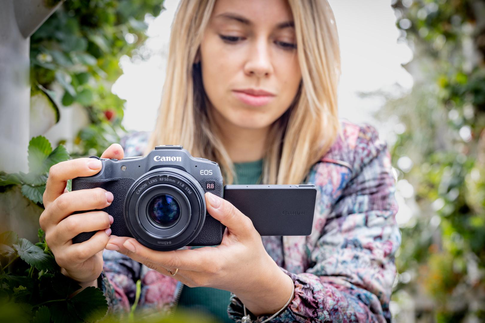 Frau hält Canon-Kamera, verschwommener grüner Hintergrund, Innenaufnahme.