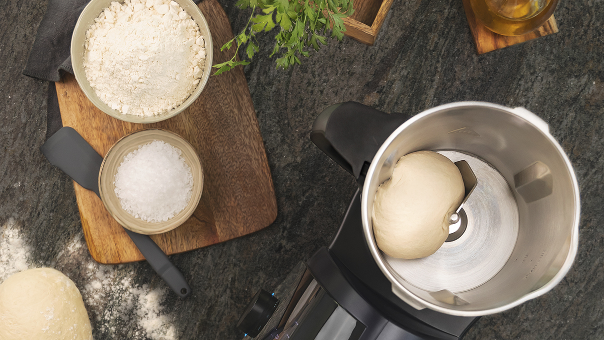 Vista cenital de masa e ingredientes en una cocina. Harina, sal y bola de masa visibles.