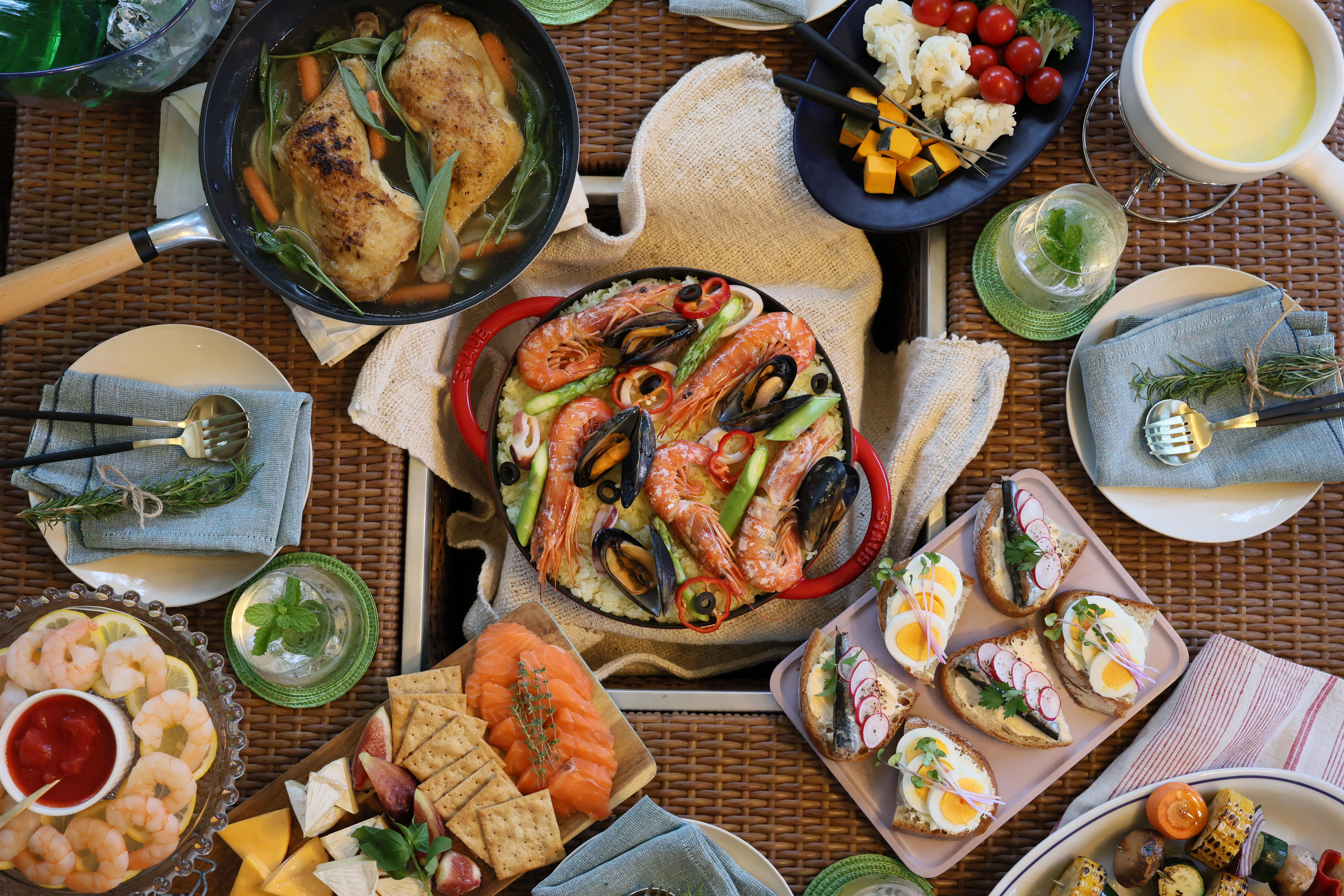 Ein Tisch für ein Festmahl mit verschiedenen Gerichten: Meeresfrüchte-Paella, gegrilltes Hähnchen, Käse, Garnelen und Vorspeisen.