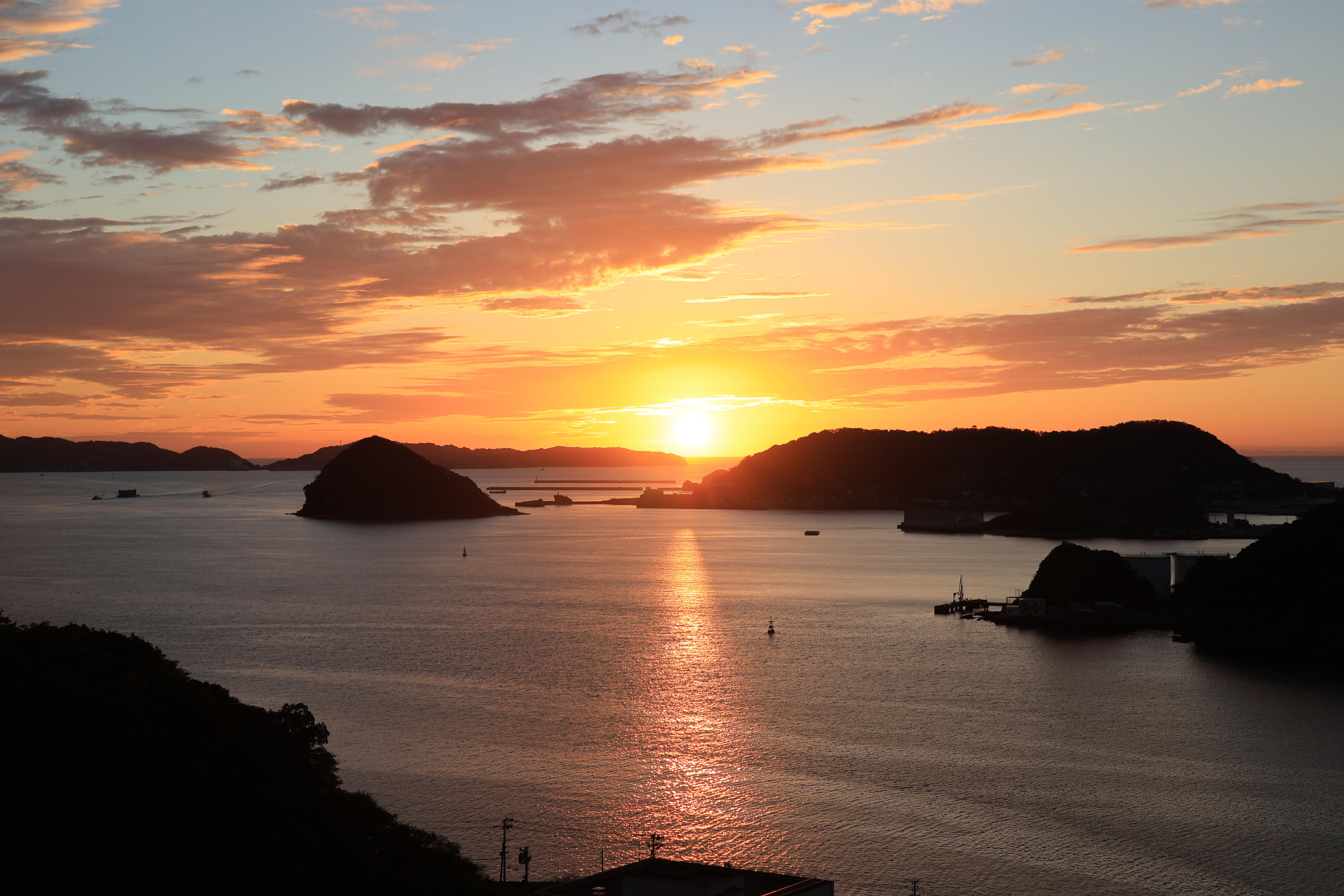 Sonnenuntergang über Wasser mit Inseln und Booten. Orange-gelber Himmel mit Sonnenreflexion.