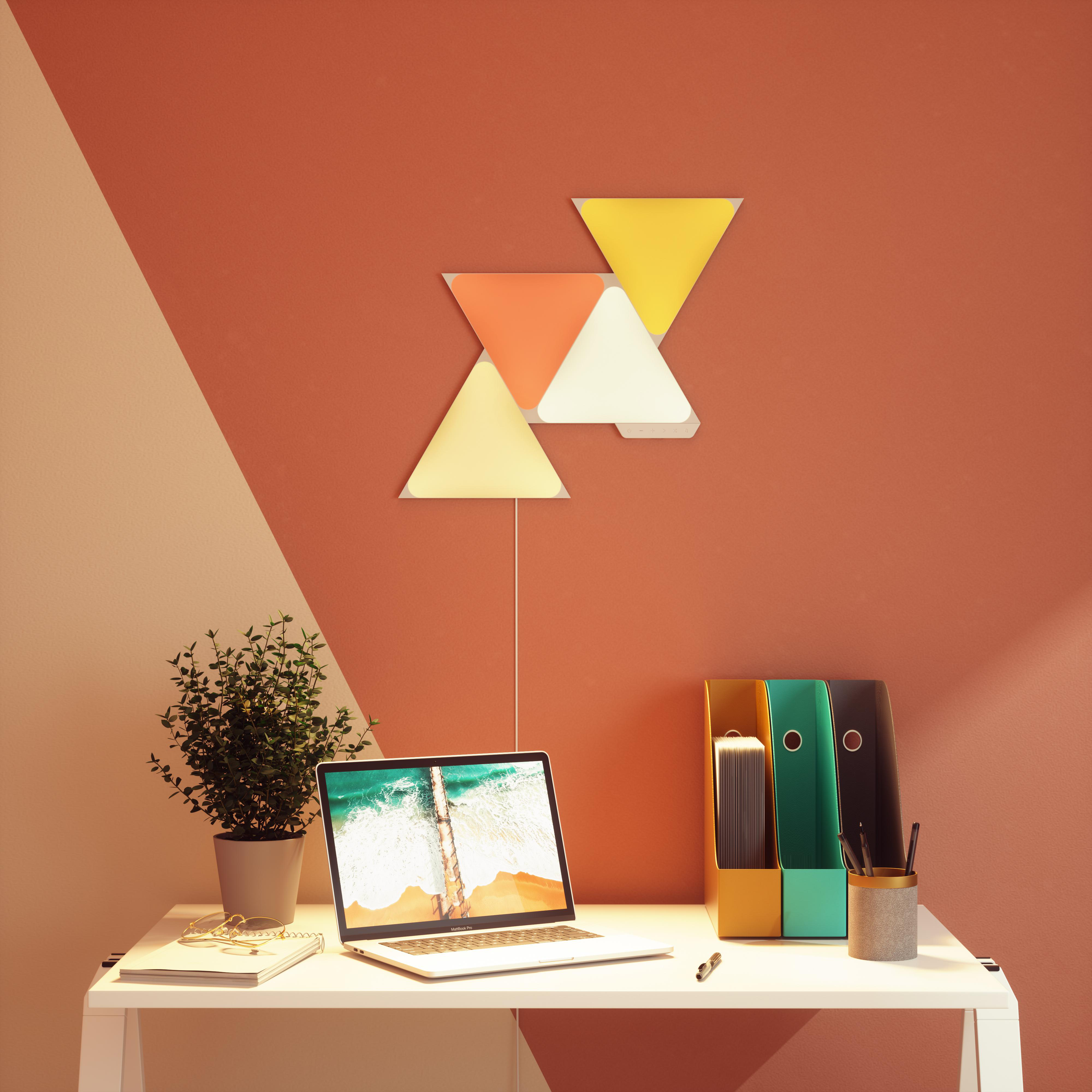 Schreibtisch-Setup mit Laptop, Pflanze und bunten geometrischen Wandleuchten.
