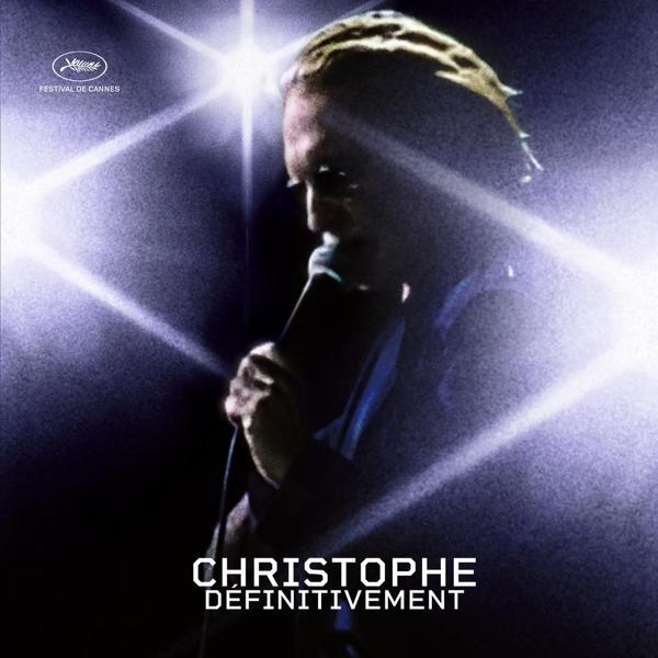 Man zingt in een microfoon op een podium met schijnwerpers, de woorden 'CHRISTOPHE DEFINITIVEMENT'.