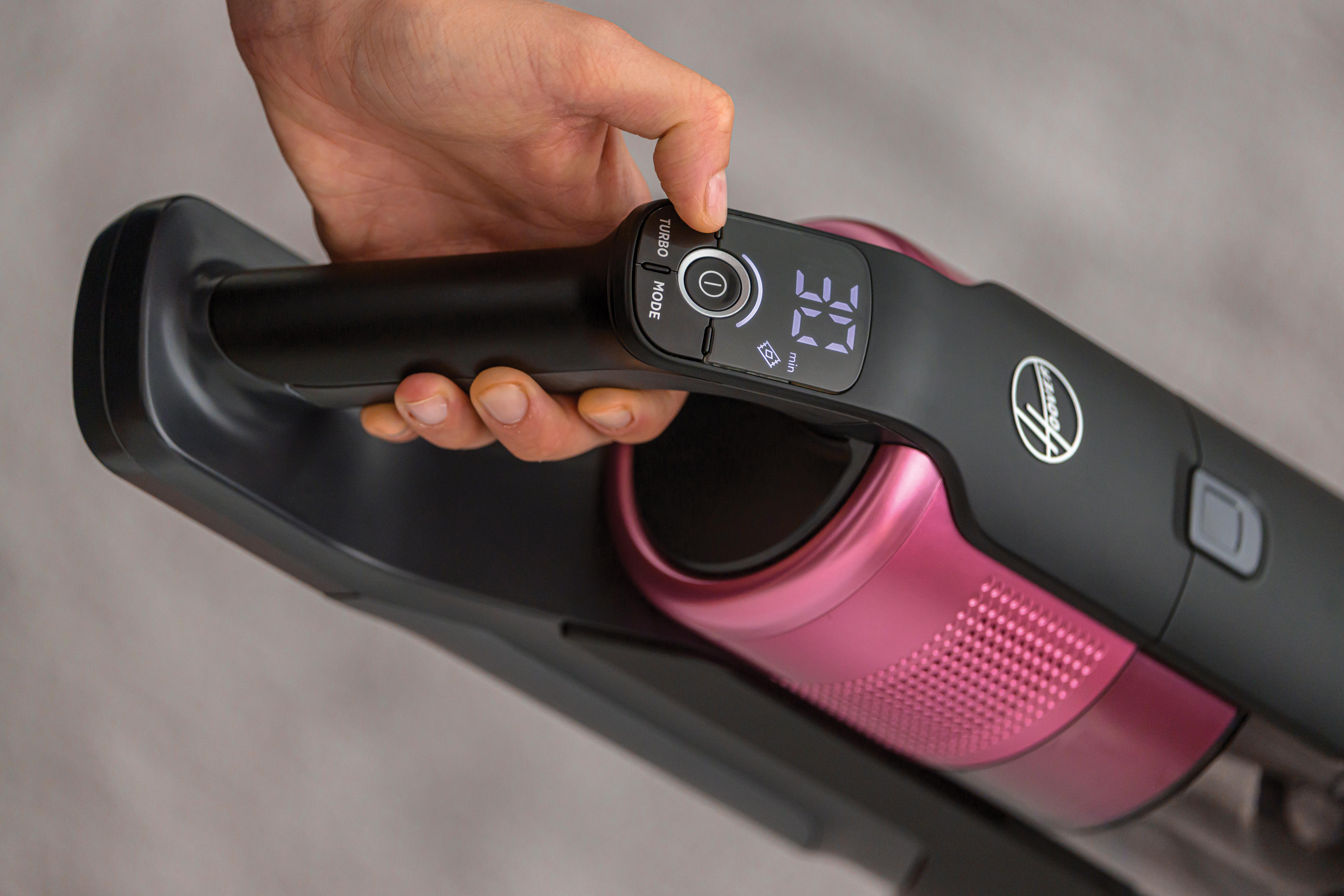 Hand drückt Knopf an einem schwarz-rosa Staubsauger.