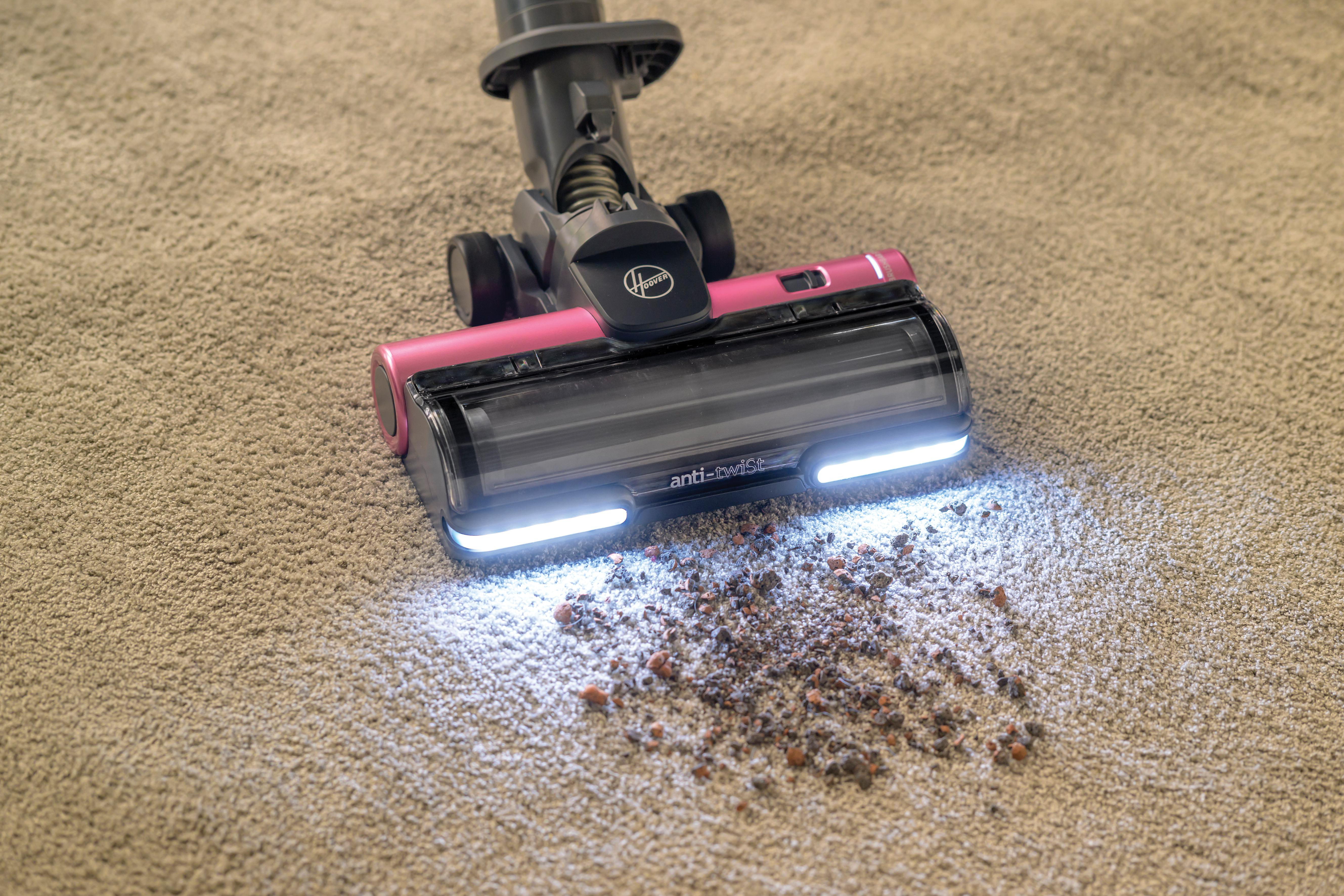 Staubsaugerkopf auf Teppich mit Schmutzhaufen, rosa und schwarz.