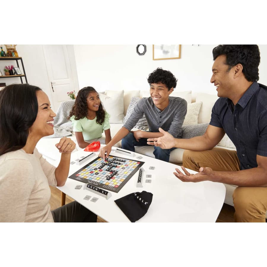 Familie spielt ein Brettspiel an einem weißen Tisch. Das Spiel ist Scrabble.