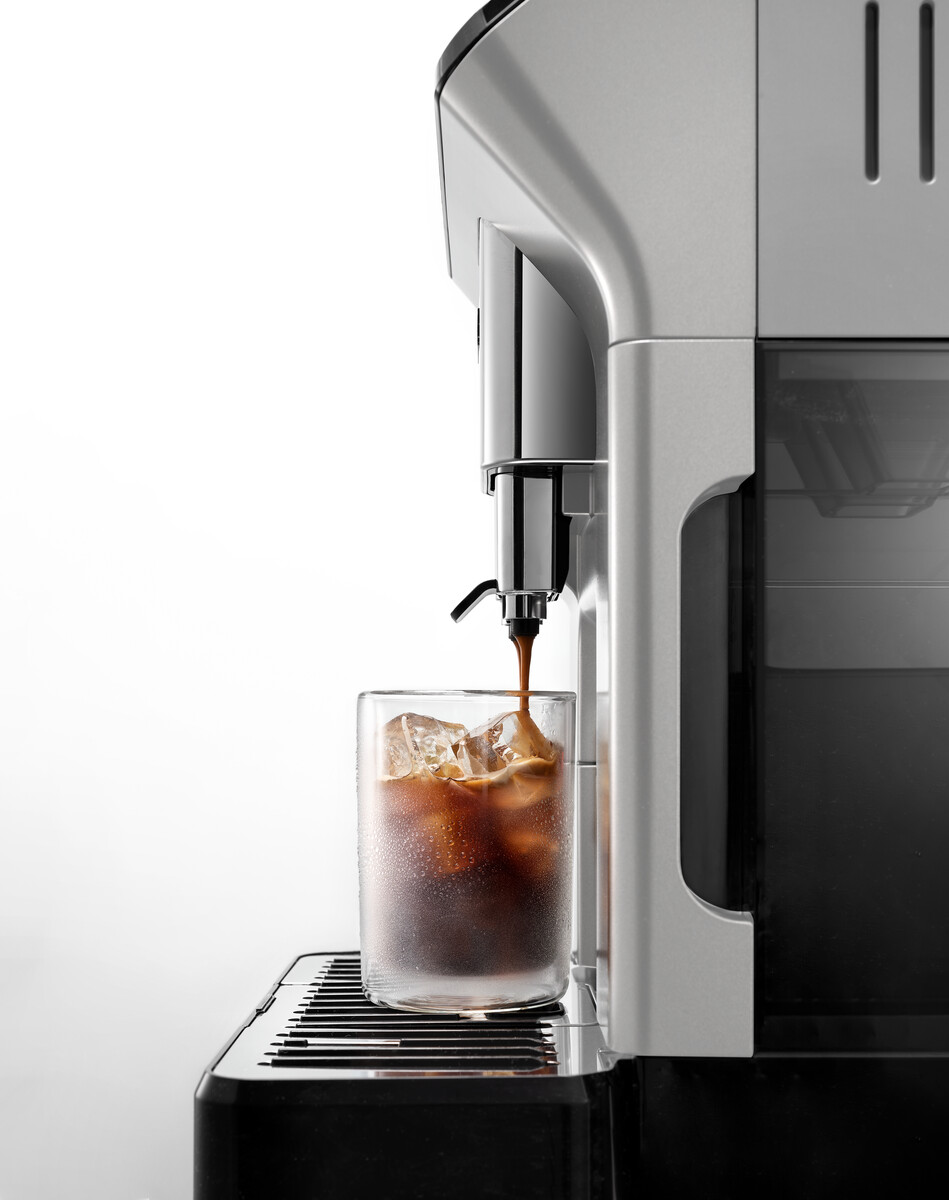 Een koffiemachine giet koffie in een glas met ijs. Witte achtergrond. Machine heeft zilveren accenten.