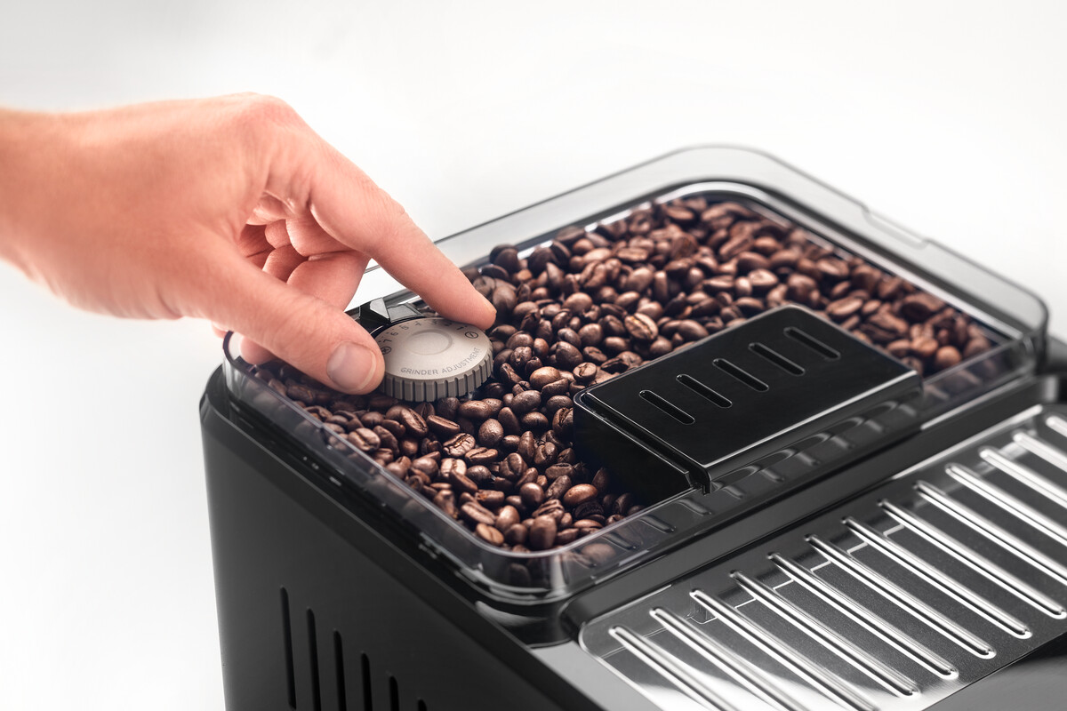 Een hand die de slijpschijf op een koffiemachine afstelt.