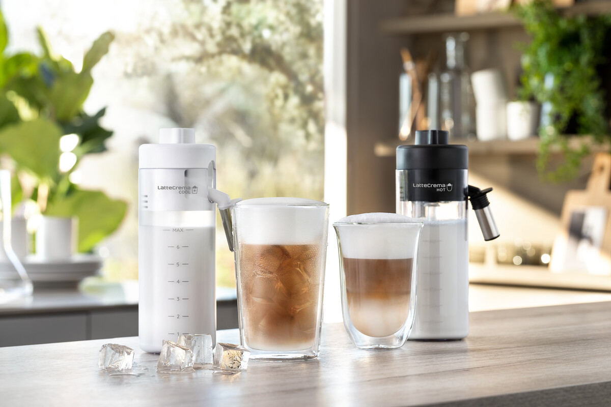 Koffiemachine met twee glazen, ijsblokjes en melkcontainers, op een houten oppervlak.