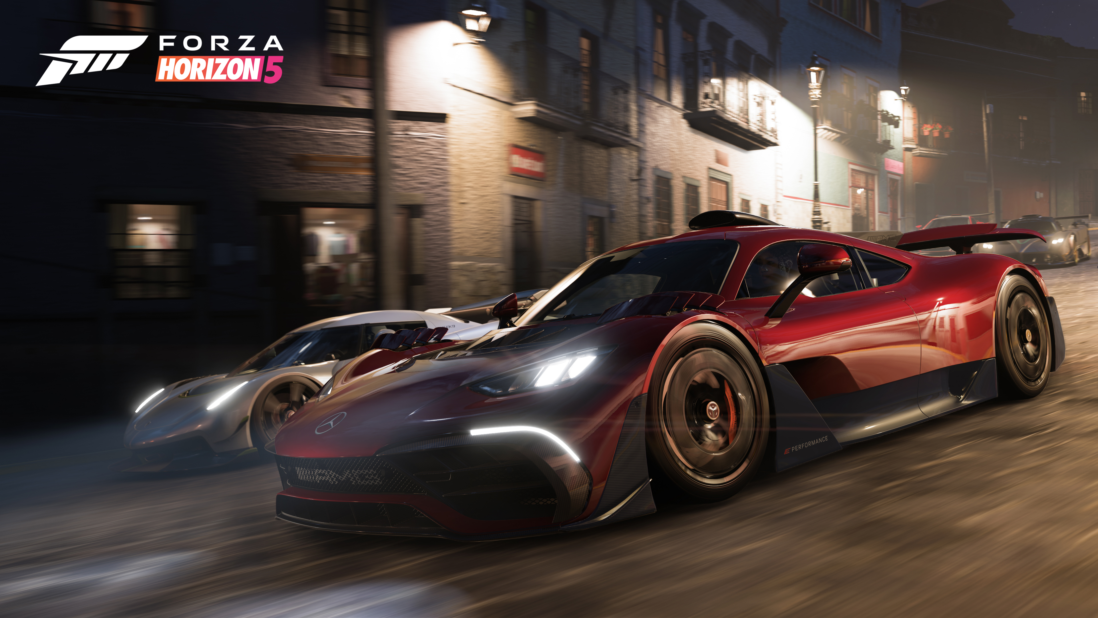 Escena del juego Forza Horizon 5. Coches deportivos rojo y plateado corriendo de noche en una calle. Faros brillantes.
