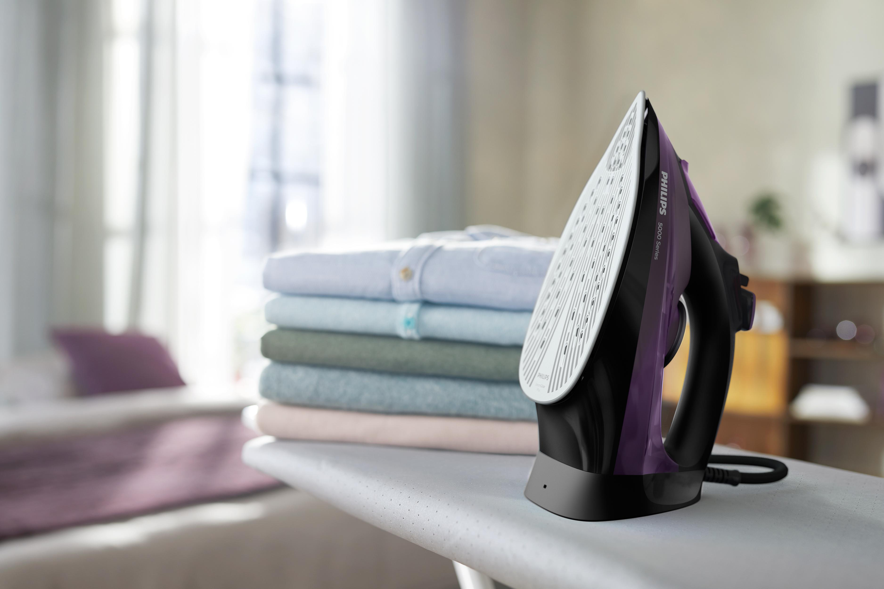 Bügelmaschine mit Bügeleisen, Kleiderstapel und unscharfem Hintergrund.