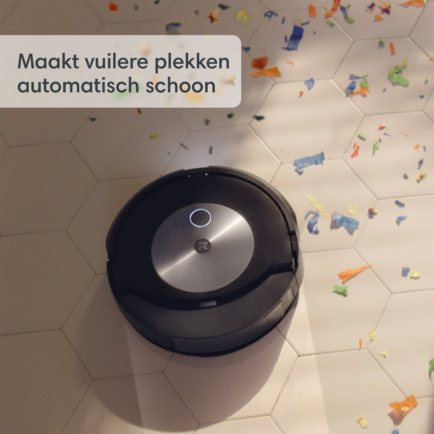 Robotstofzuiger op een tegelvloer met confetti. Tekst: 'maakt vuile plekken automatisch schoon'.