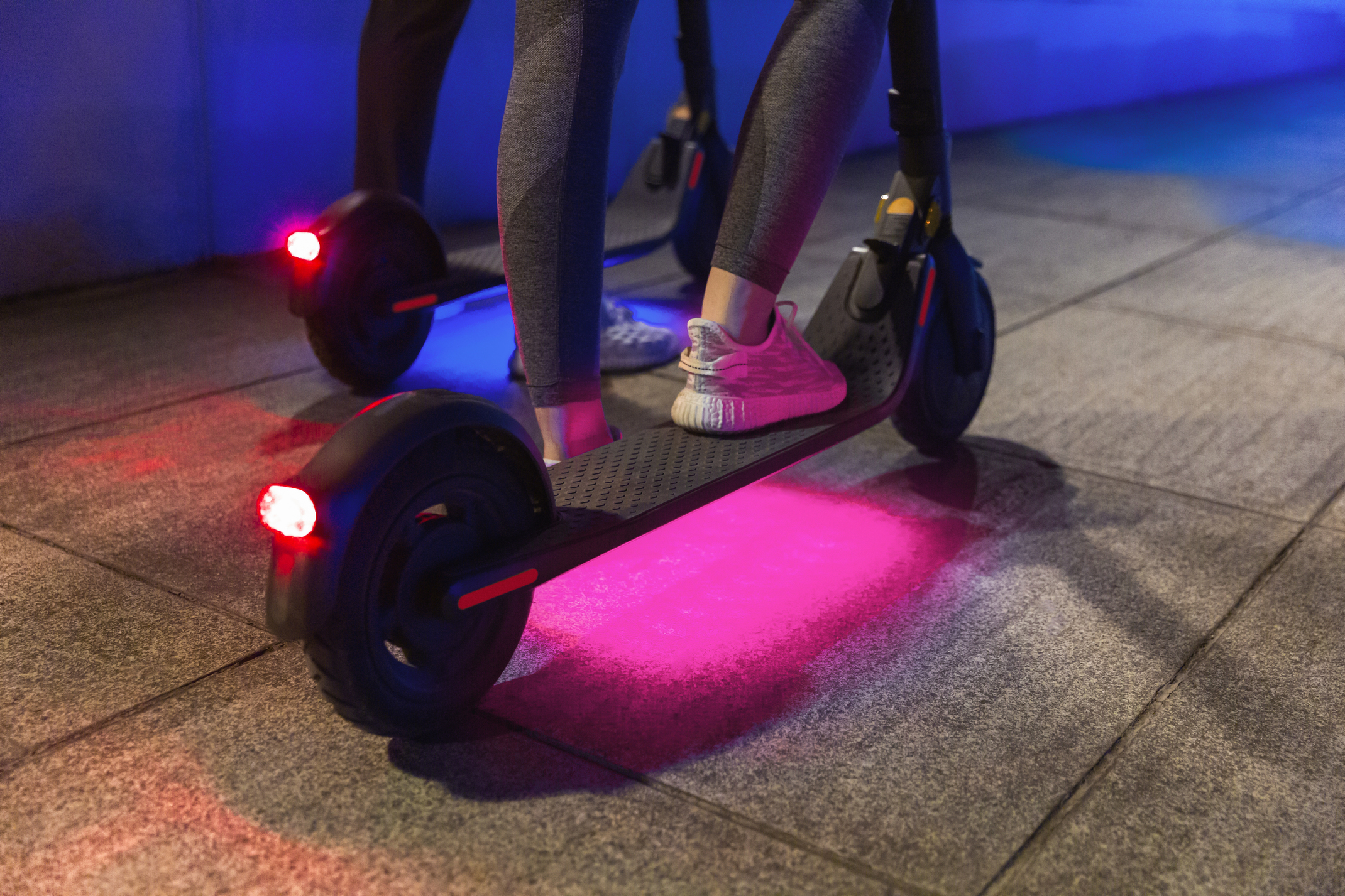 Kırmızı ışıklı, gece elektrikli scooter kullanan iki kişi.