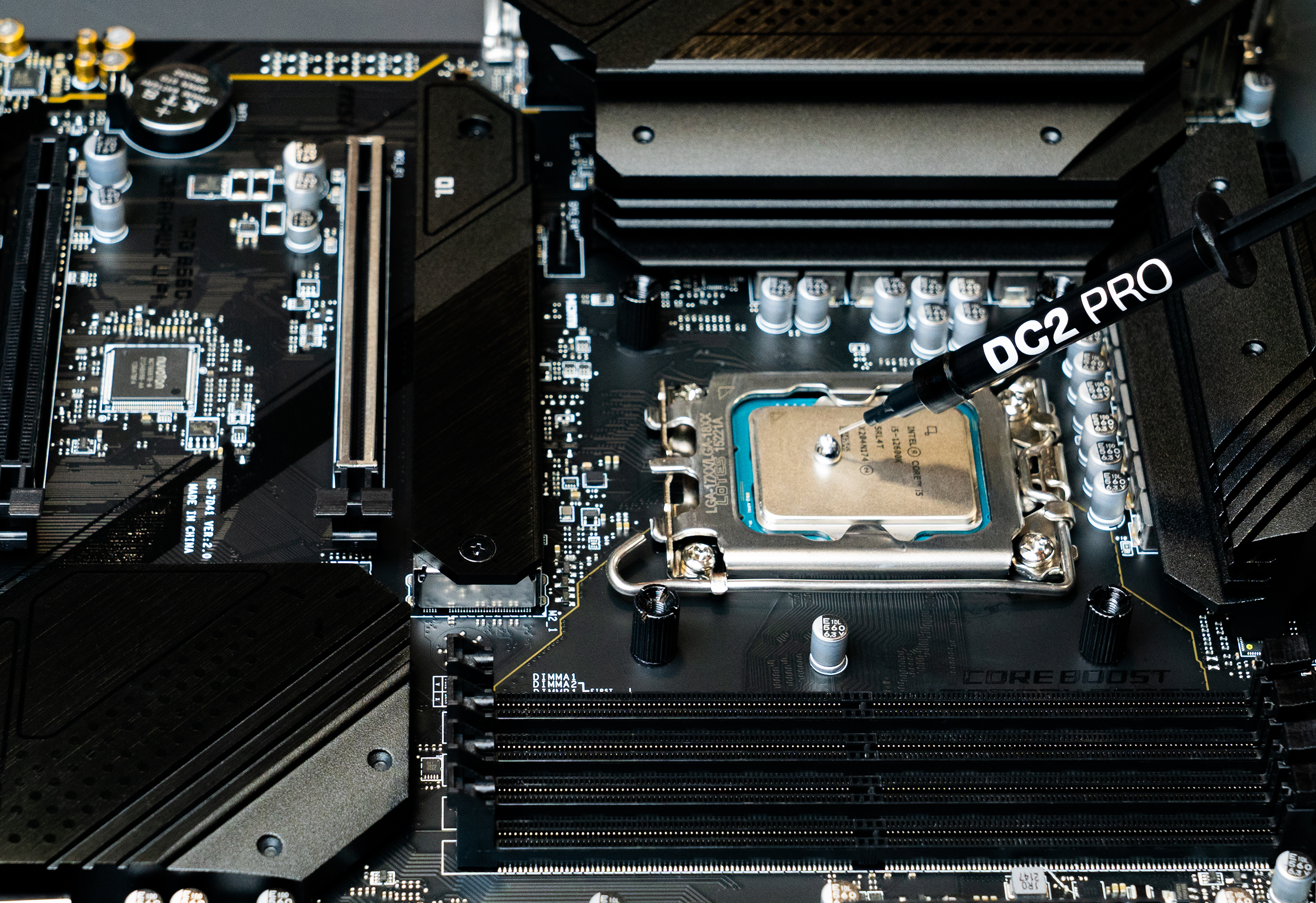 Nahaufnahme eines Motherboards, auf das mit einer Spritze Wärmeleitpaste auf die CPU aufgetragen wird.