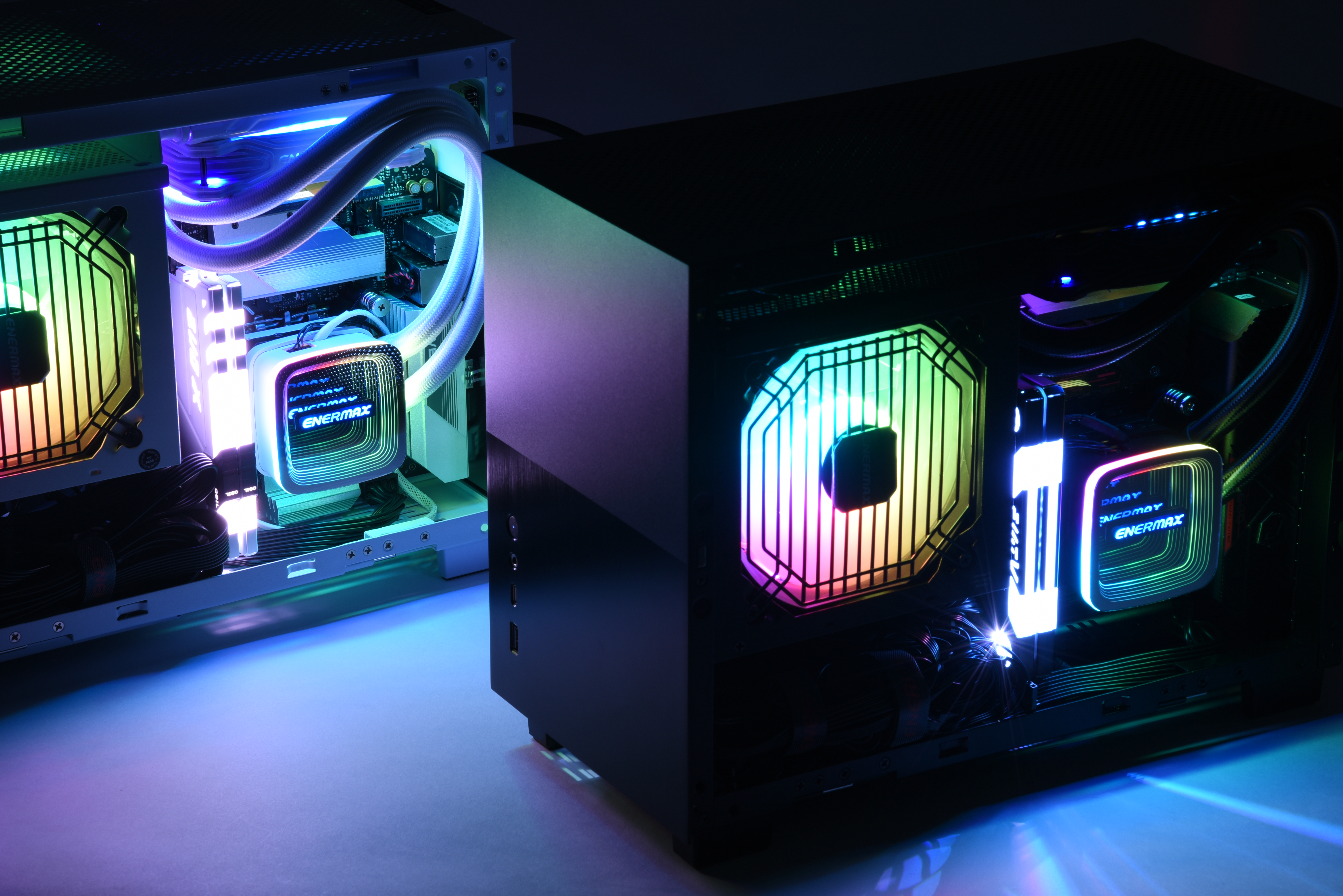 Zwei Computer mit Wasserkühlung, Lichtern, dunklem Hintergrund, farbenfrohes Leuchten.