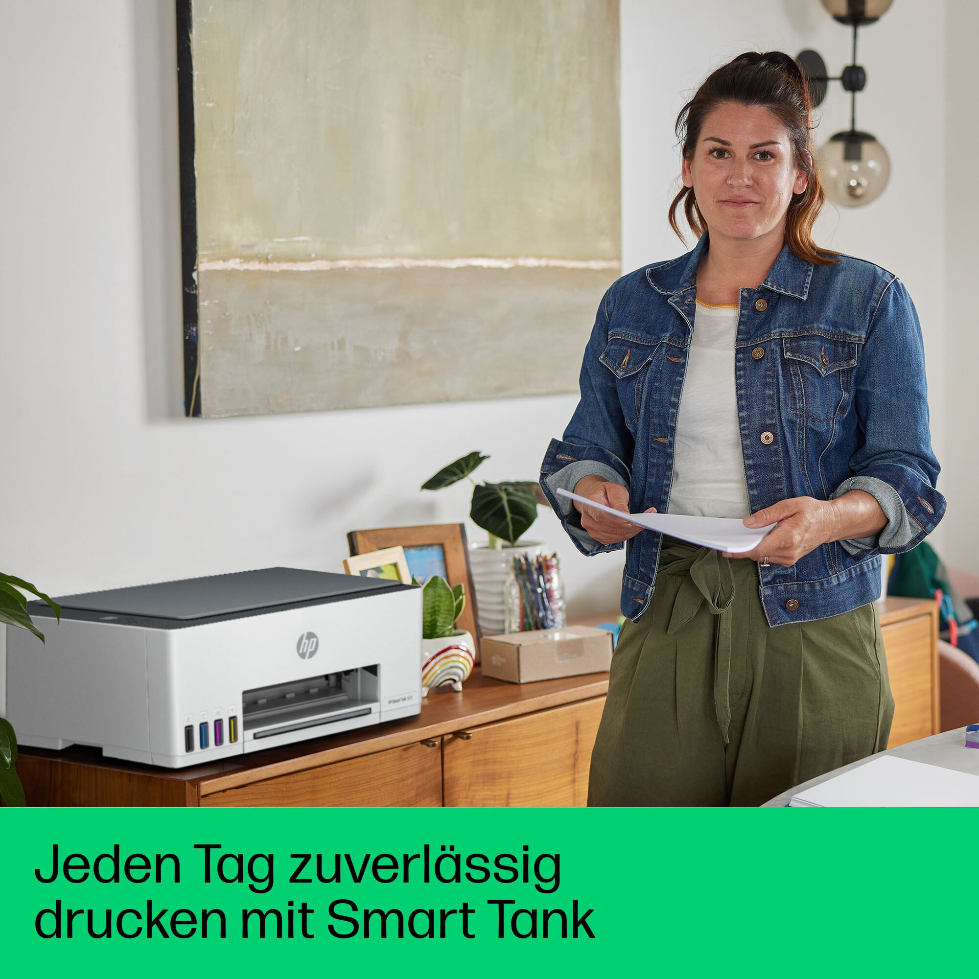 Frau mit Papieren steht neben einem Drucker auf einem Holzschrank, ein Gemälde hängt an der Wand.