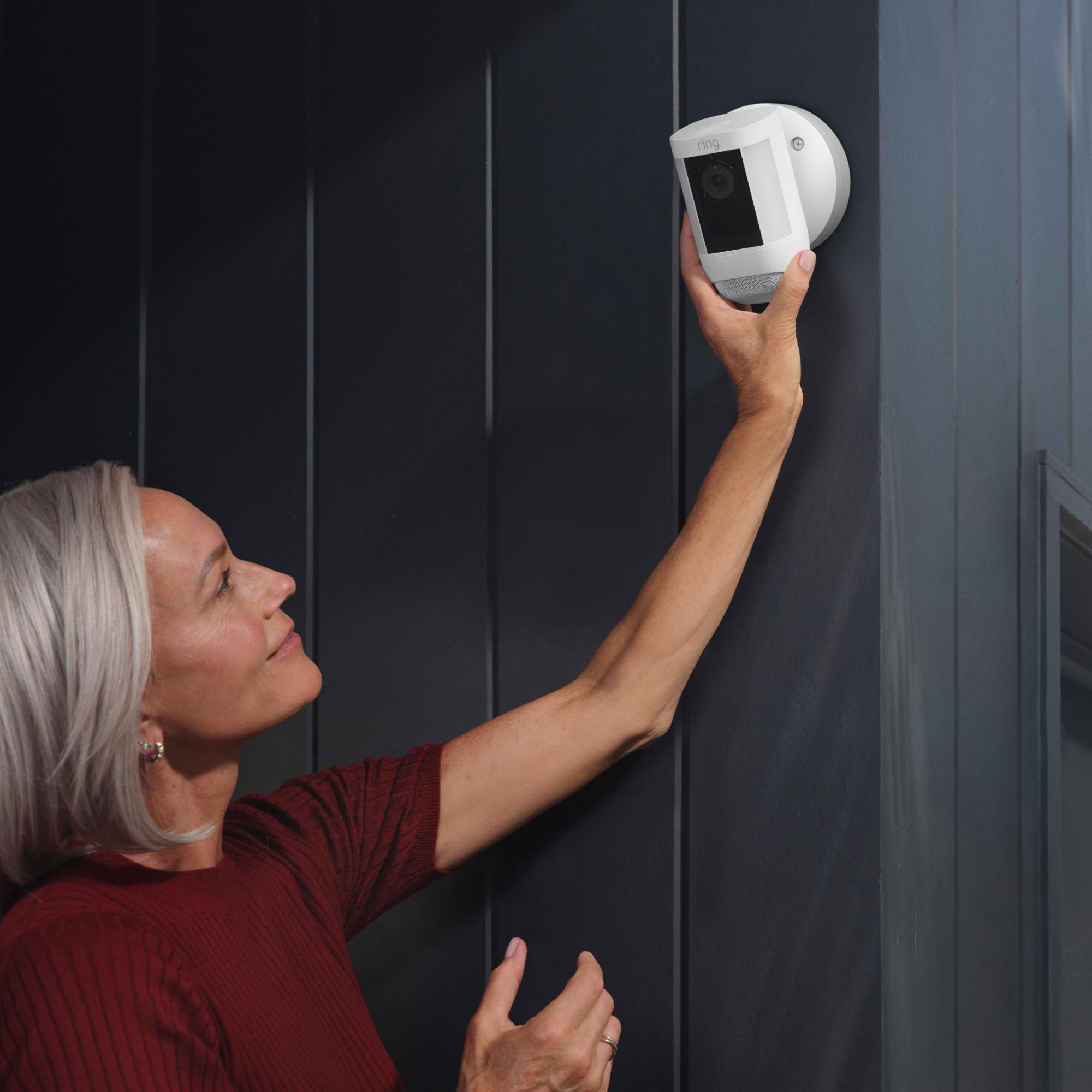 Eine Frau installiert eine weiße Überwachungskamera an einer dunklen Wand.