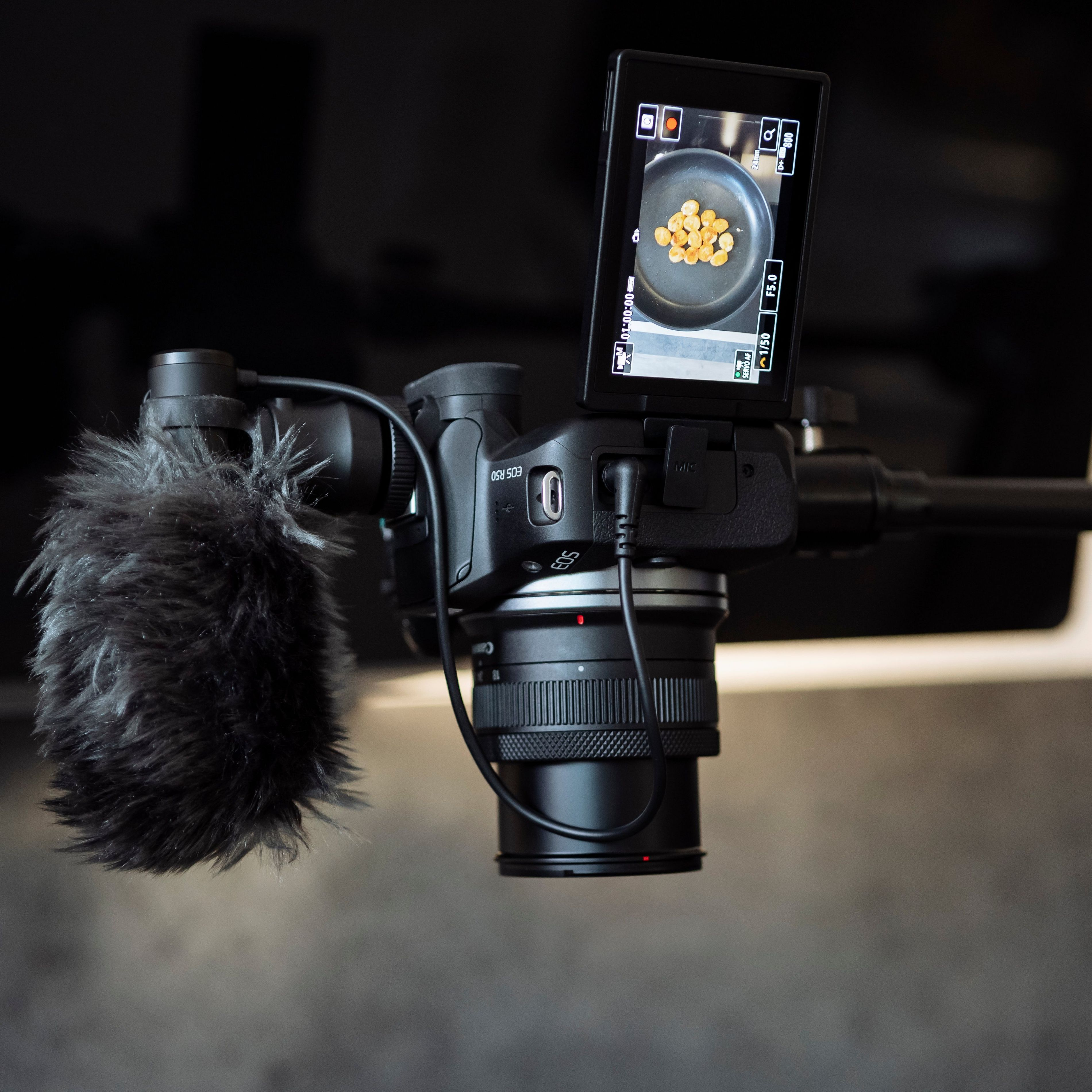 Kamera-Setup mit Mikrofon und Bildschirm. Der Bildschirm zeigt Essen, das in einer Pfanne gekocht wird.