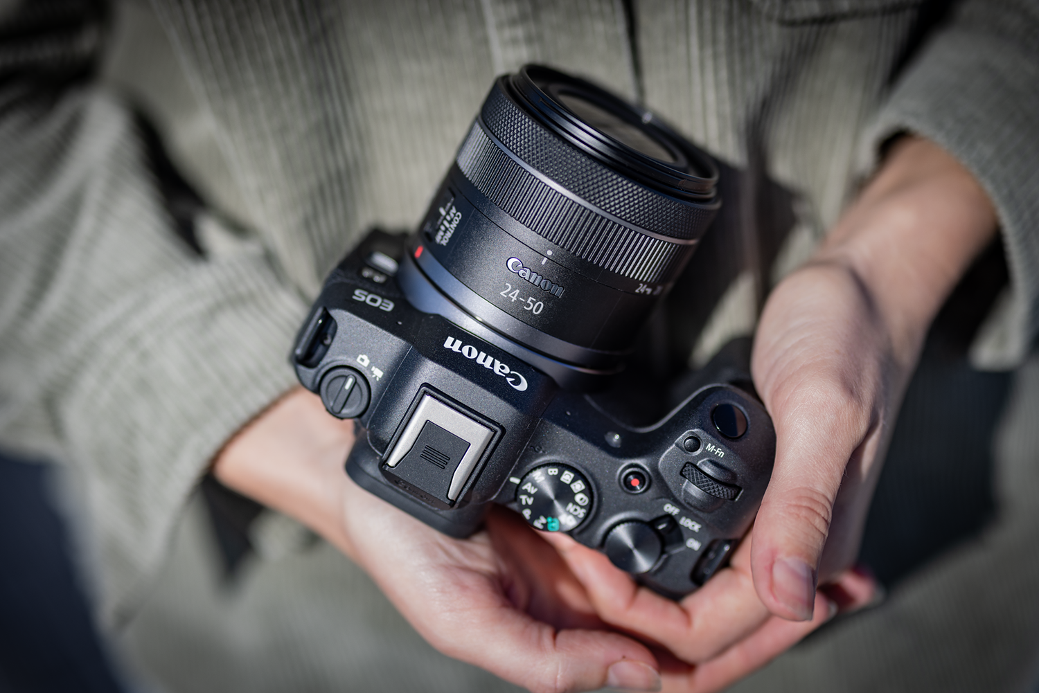 A person holding a black Canon camera with a lens.